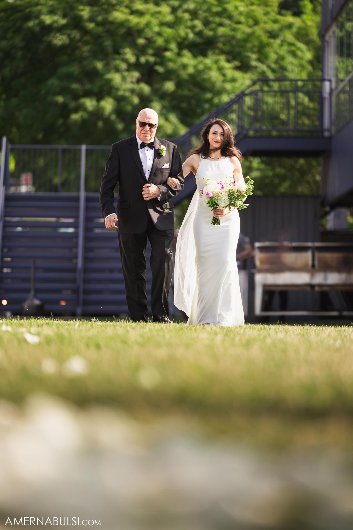 A traditional wedding processional moment captured in a sunlit garden setting.