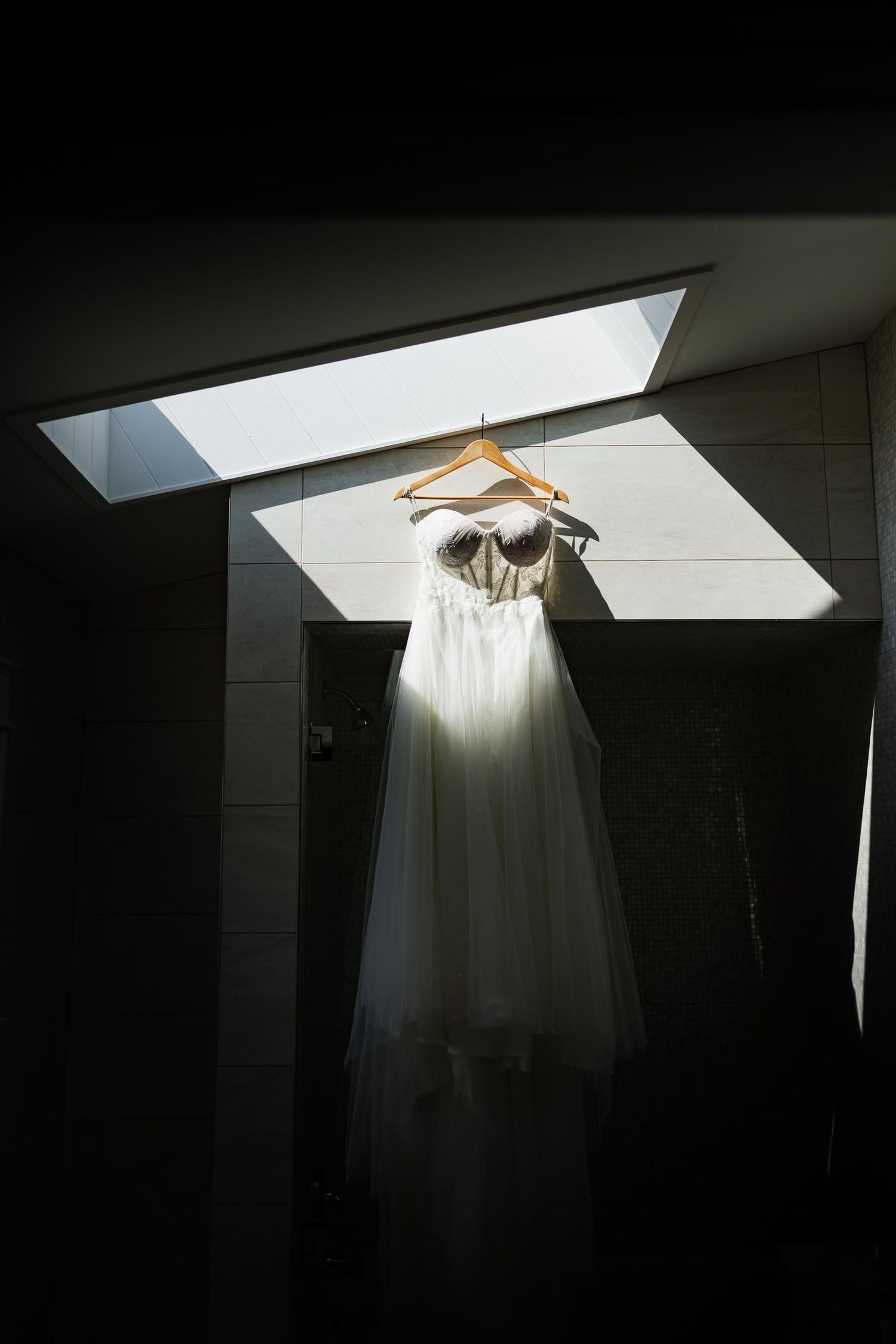 Wedding dress on hanger illuminated by natural light through skylight.