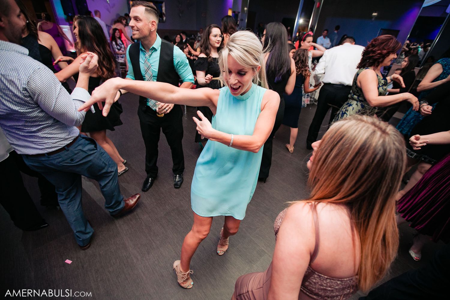Party guests dance and celebrate on a dark dance floor illuminated with ambient lighting.