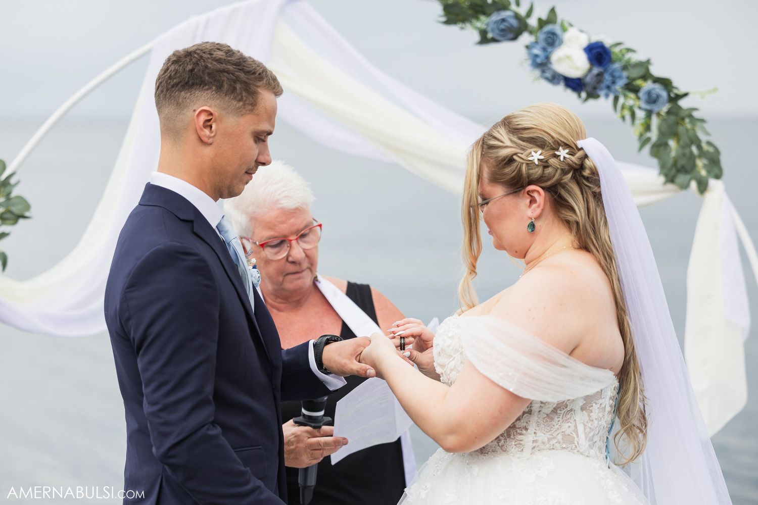 Romantic seaside wedding ceremony moments with floral arch and blue sky backdrop.
