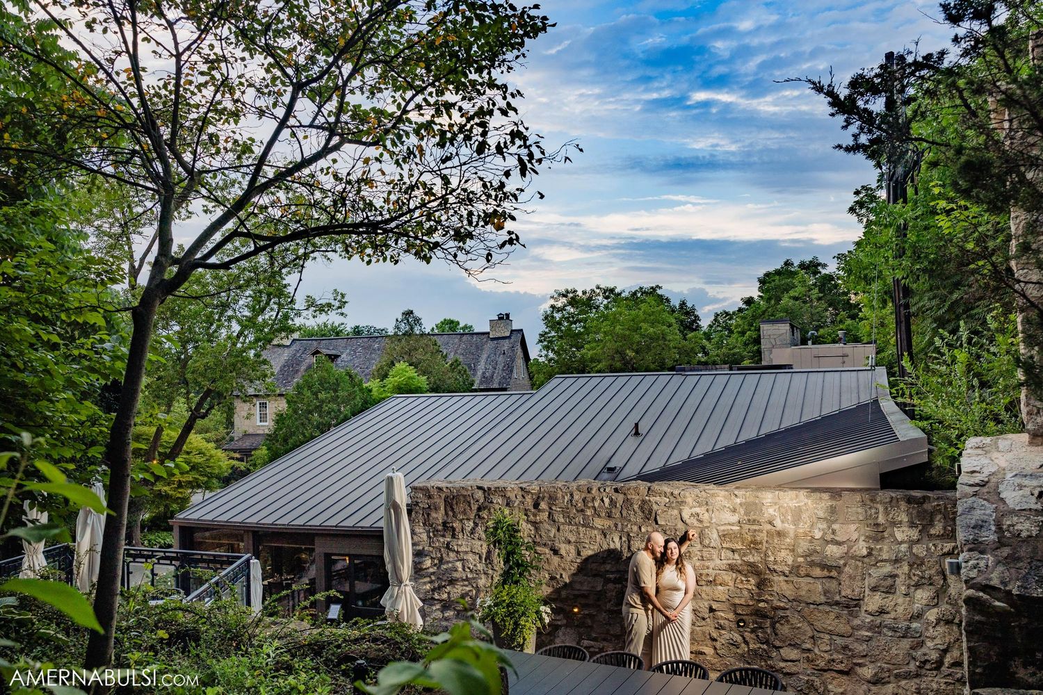 Stone chapel with metal roof nestled among trees under blue skies.