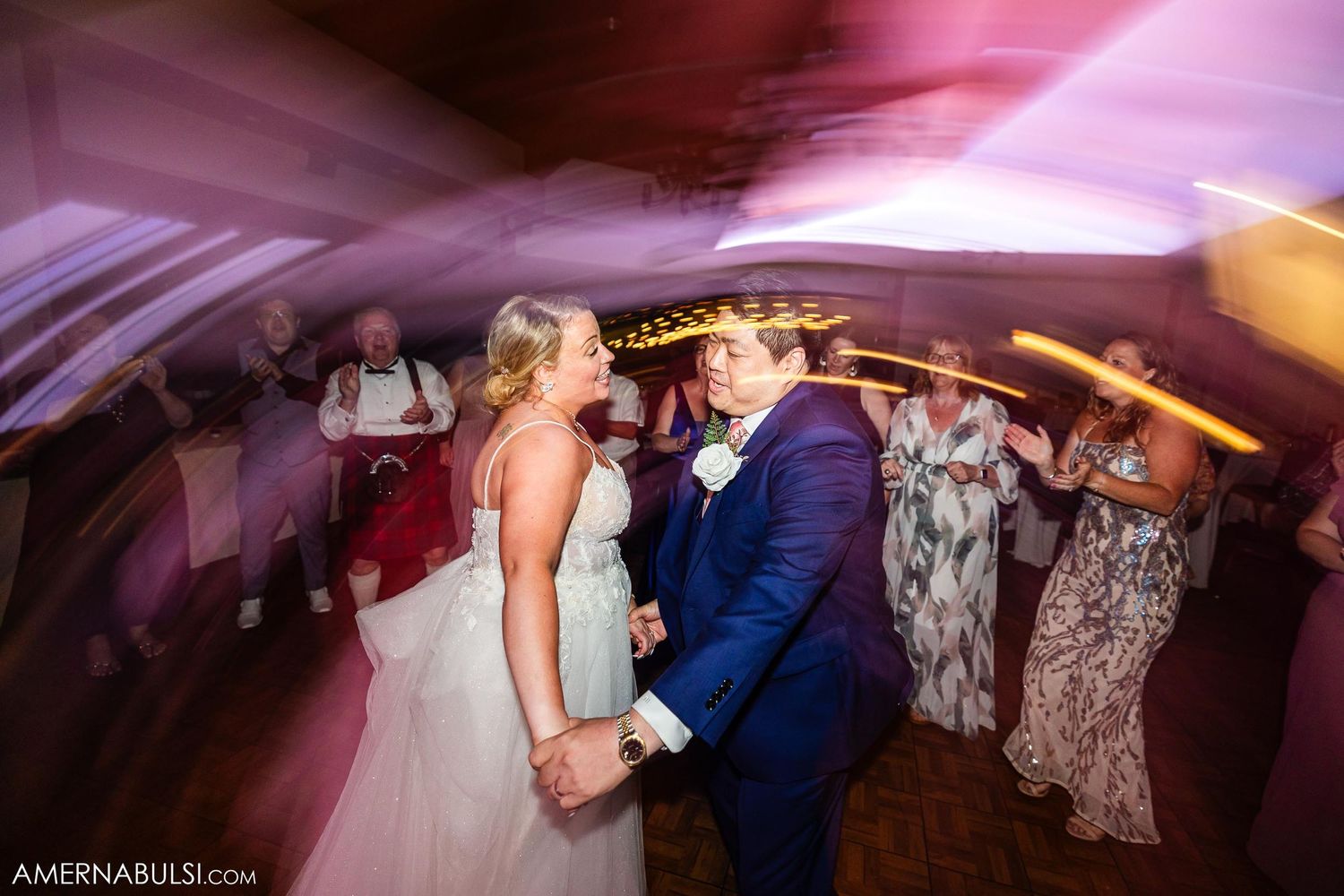 Dance floor moment at wedding reception with atmospheric pink lighting and motion blur.