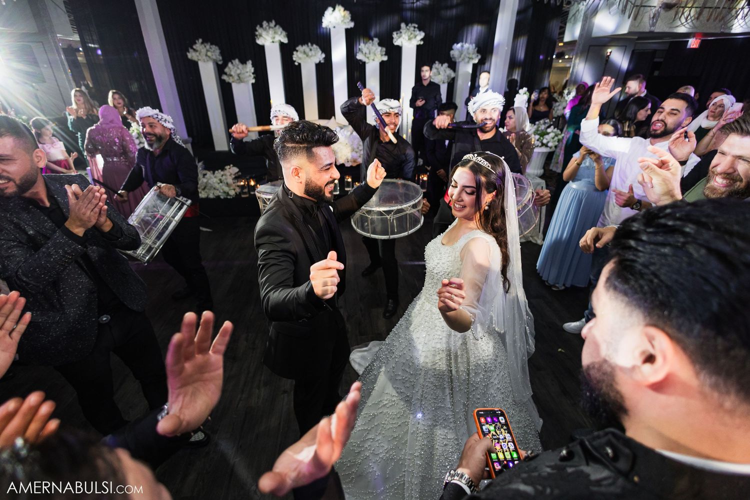 Lively wedding reception with guests dancing under decorative lighting.