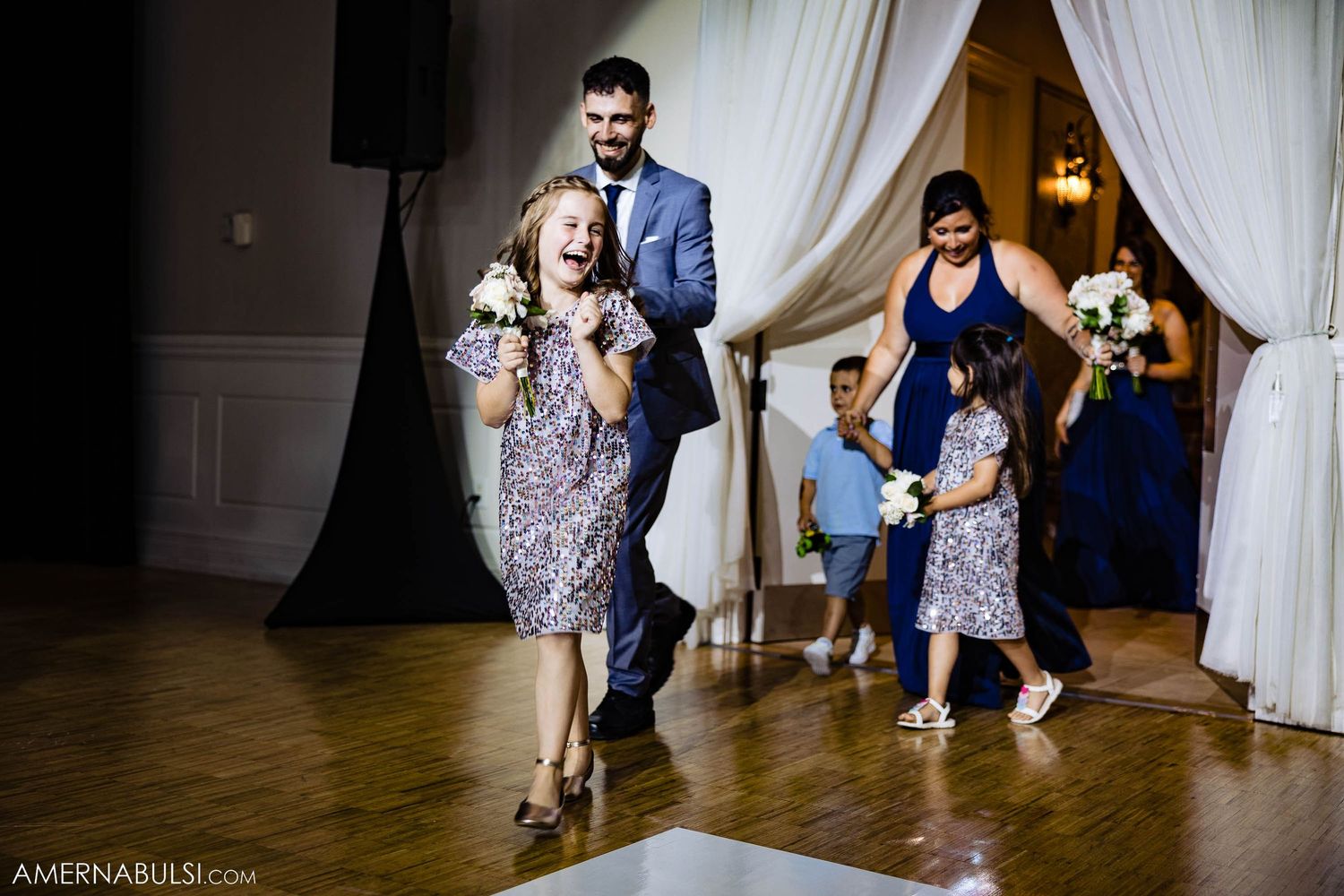 Wedding party dances in coordinated navy and grey attire during reception celebration.