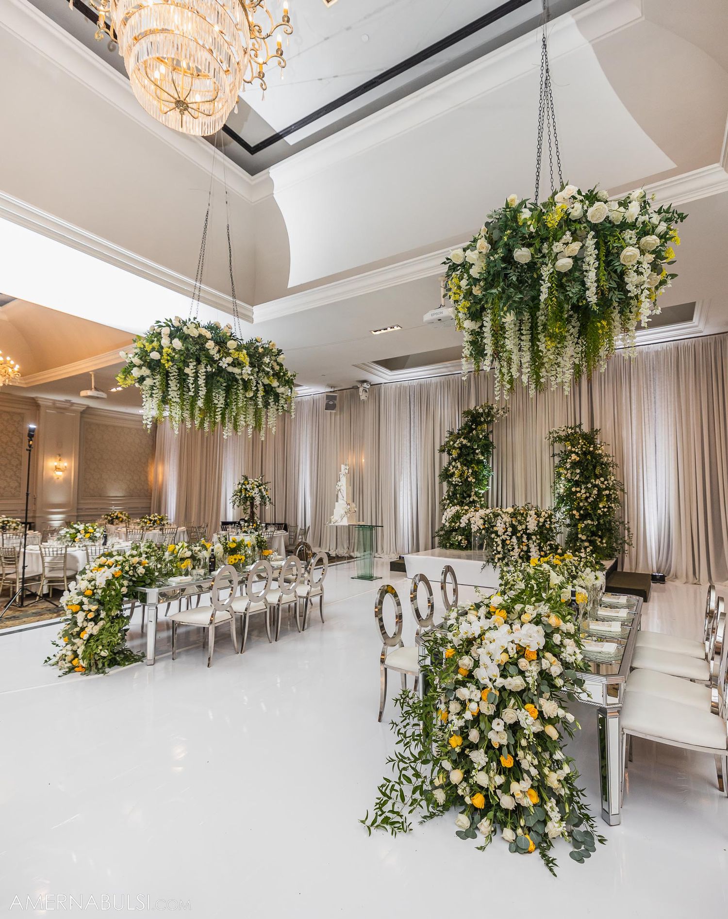 Luxurious wedding reception setup with hanging floral installations and white decor elements.