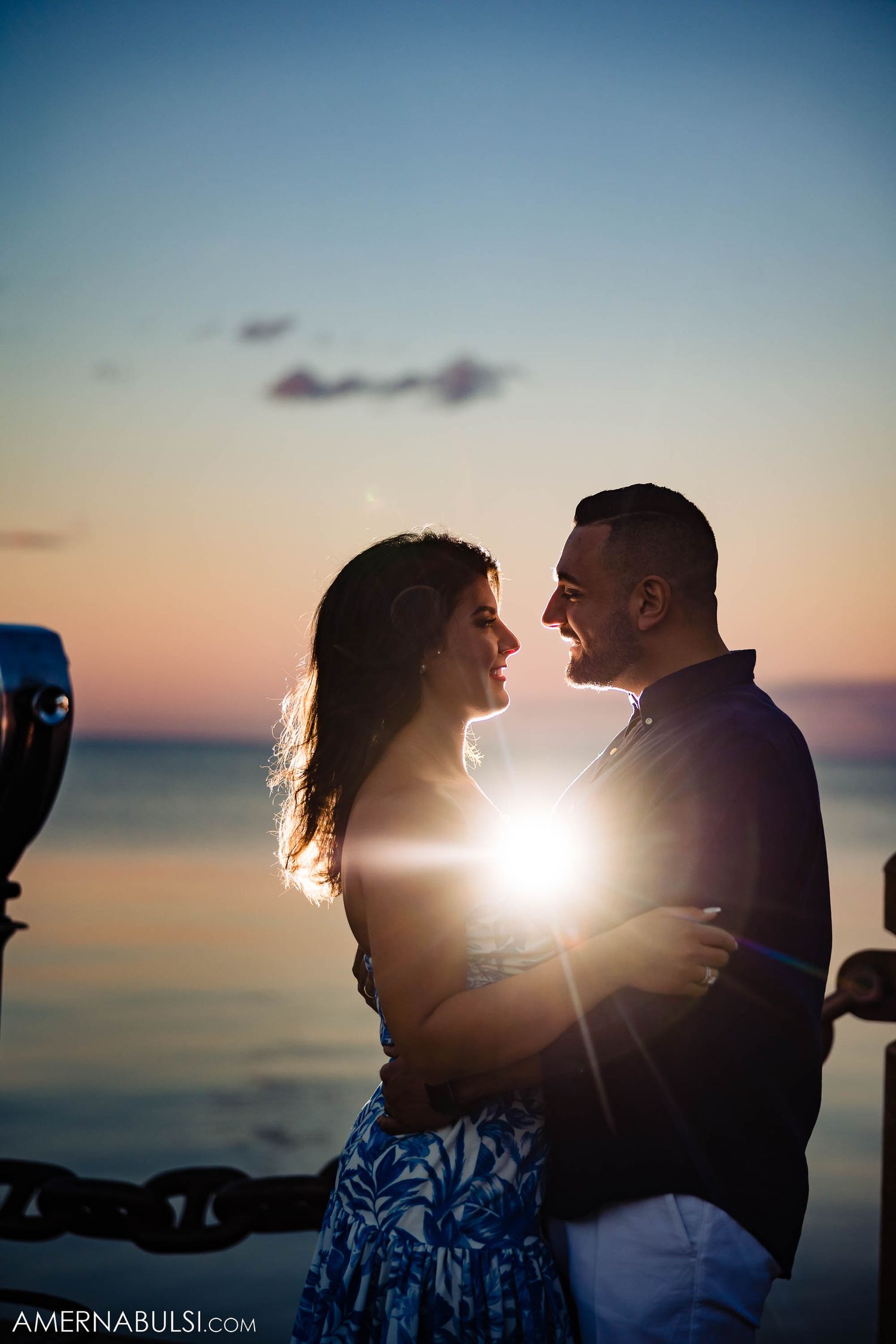 Romantic silhouette of a couple embracing at sunset by the ocean with a lens flare between them.
