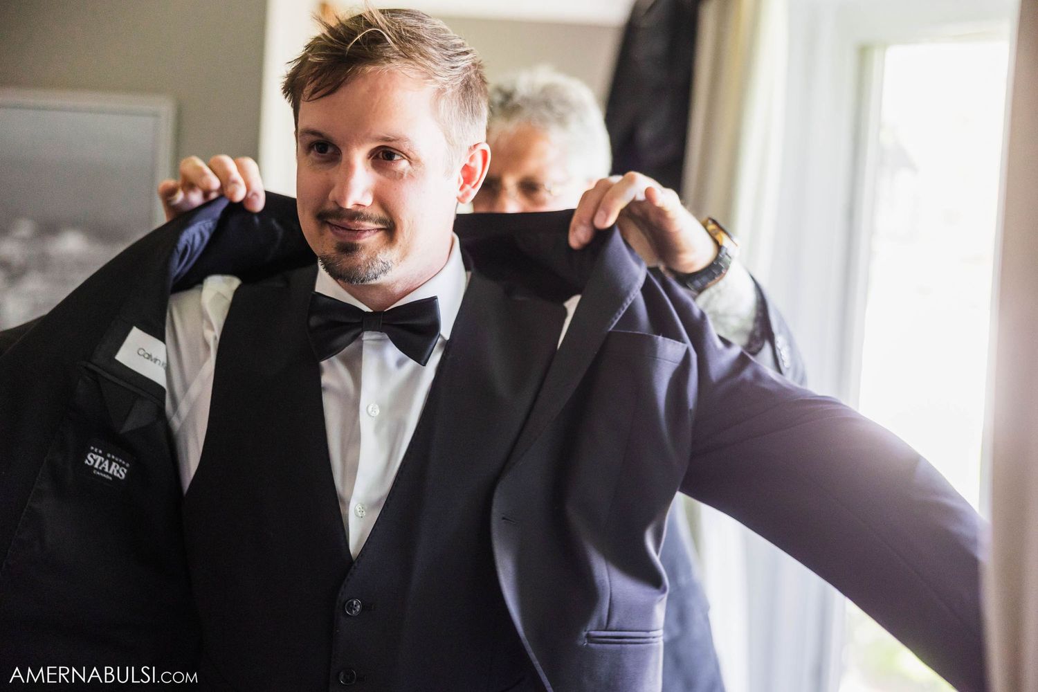 Person adjusting bowtie while getting ready in formal attire before wedding ceremony.