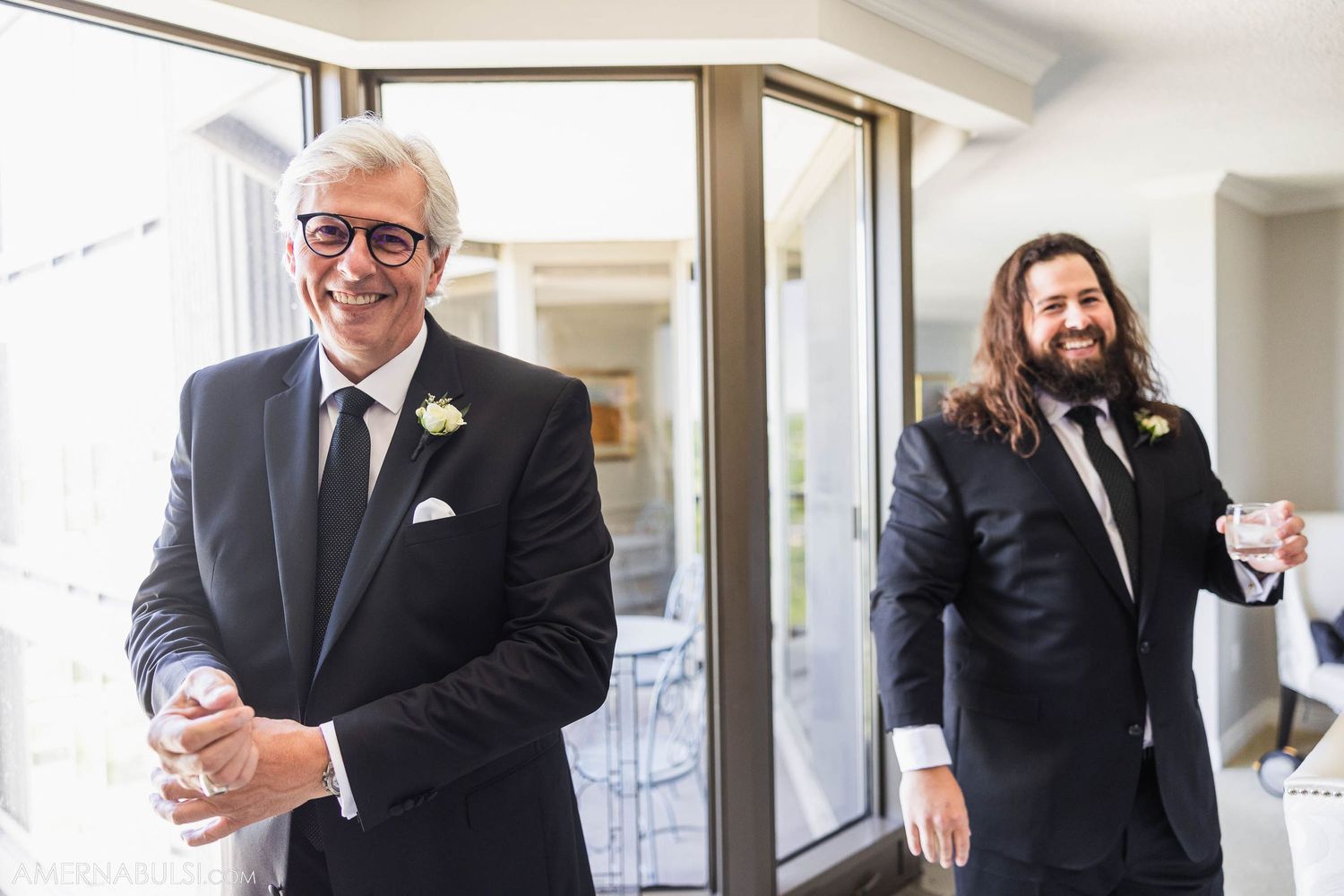 Wedding party members in formal suits sharing a light moment indoors.