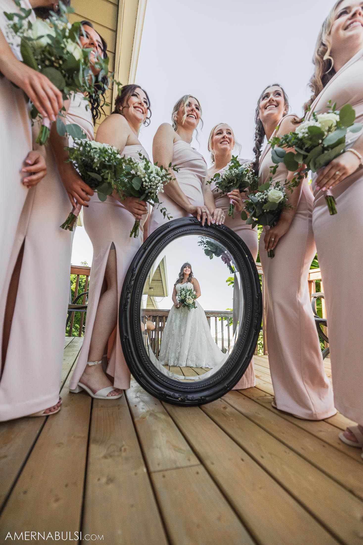 Creative wedding party photo using a round mirror to frame the bride while bridesmaids hold bouquets.