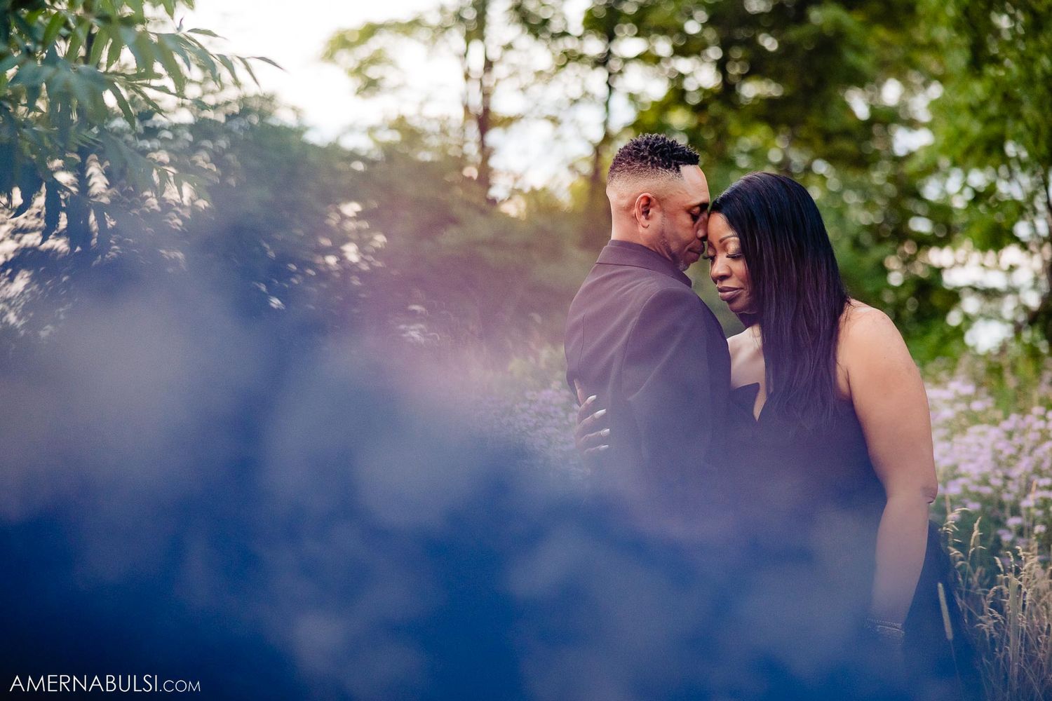 Intimate romantic portrait framed by soft bokeh and natural foliage.