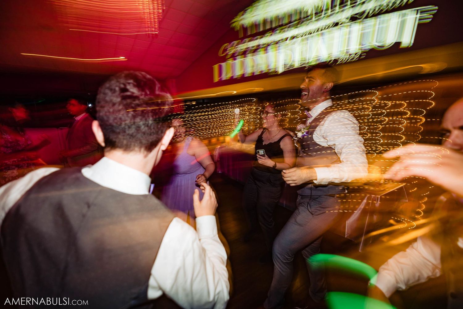 Motion-blurred dance floor scene at a lively reception with guests dancing under red lighting.