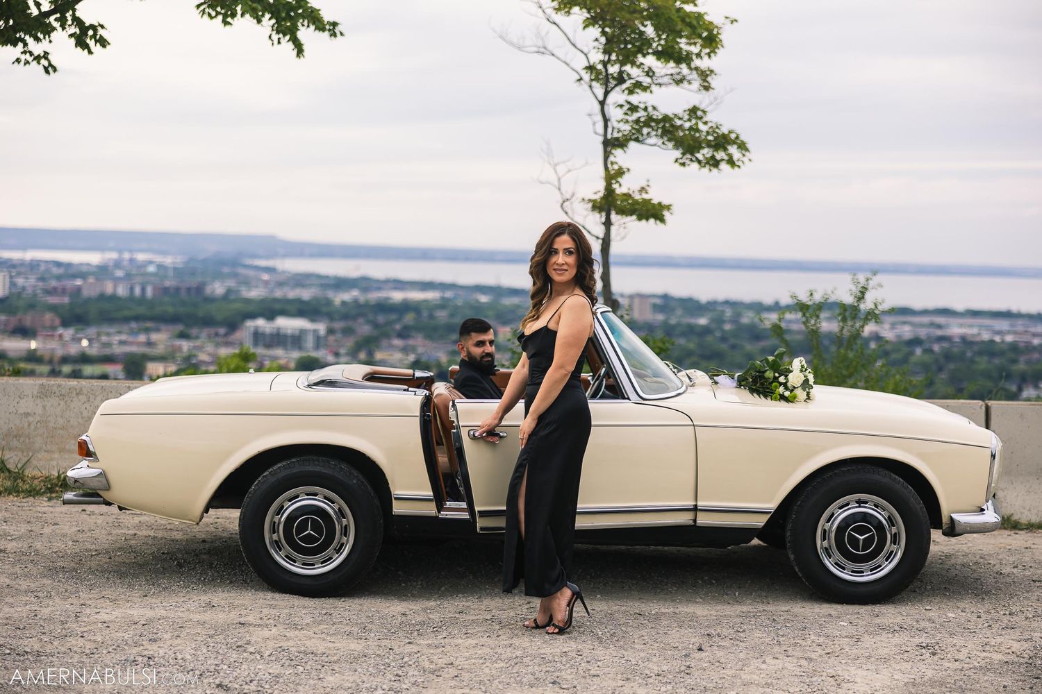 Elegant pose with classic white Mercedes-Benz convertible overlooking city vista.