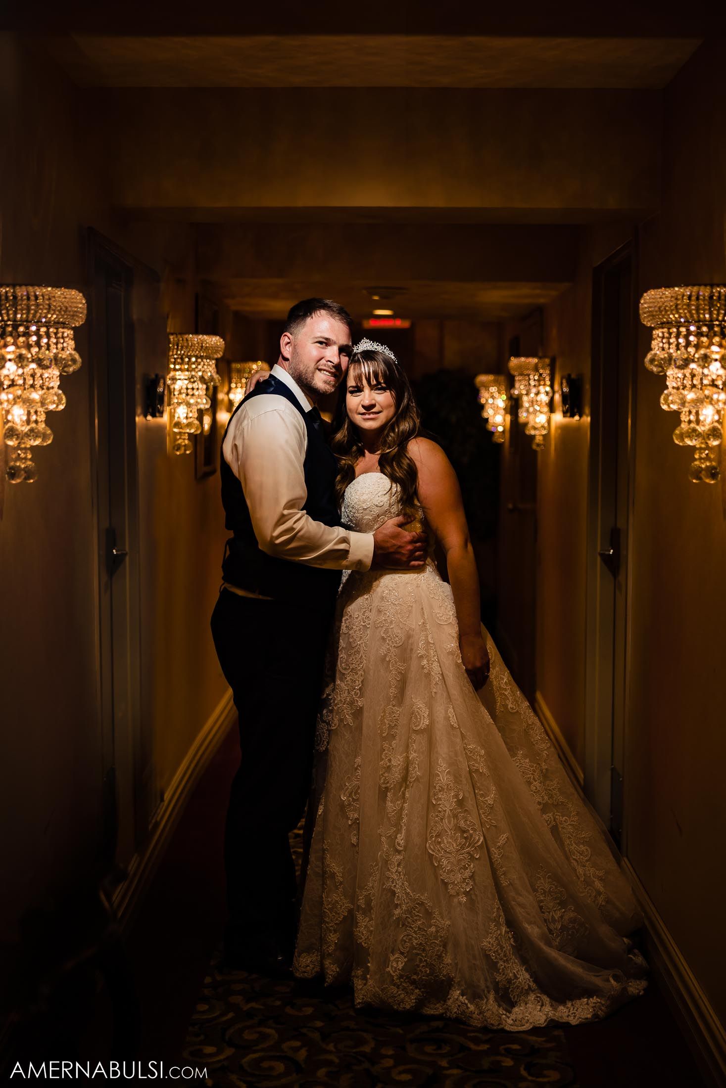 Elegant wedding portrait in a dimly lit hallway with crystal chandeliers.