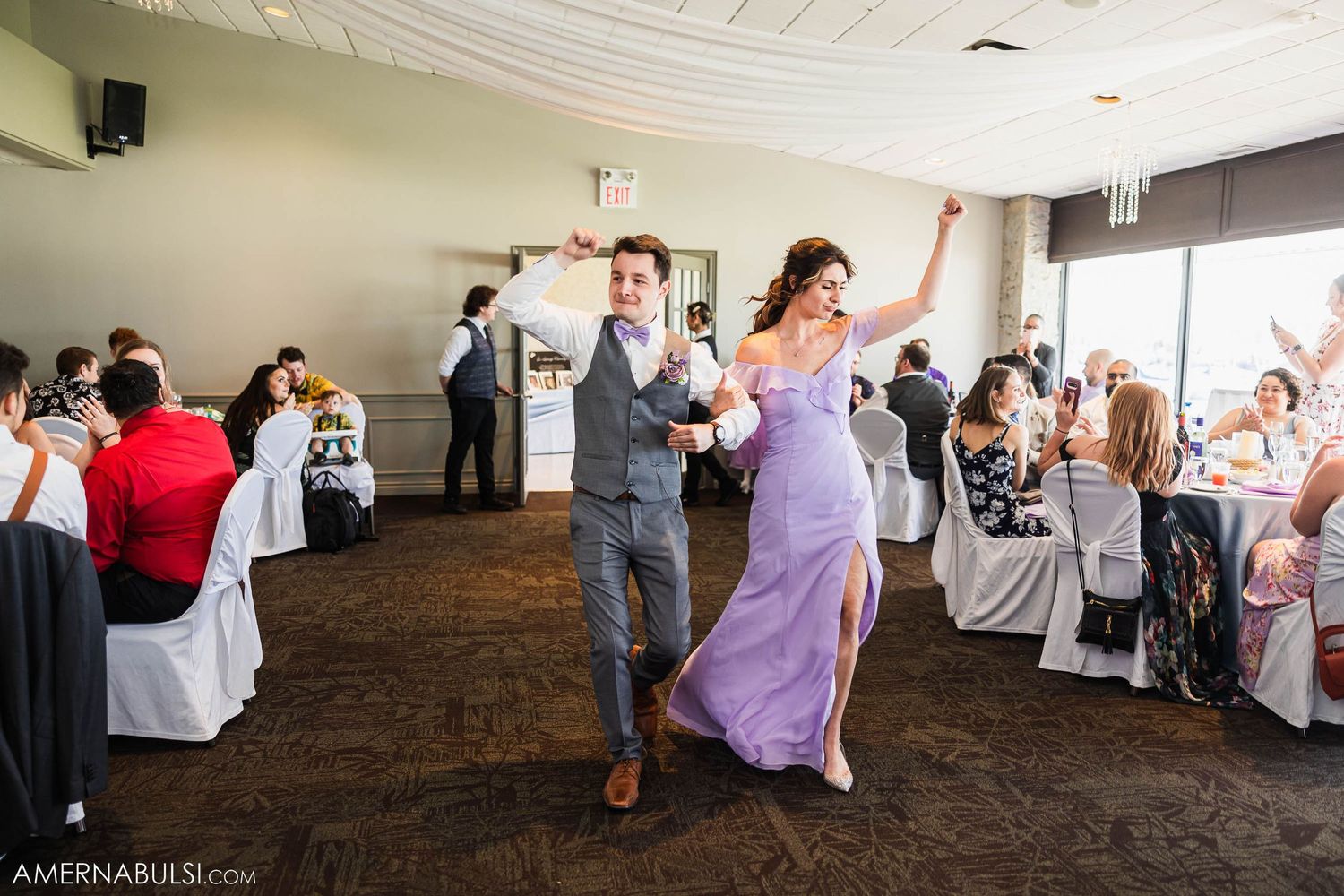 Wedding reception features celebratory dancing in indoor venue with white chair covers.