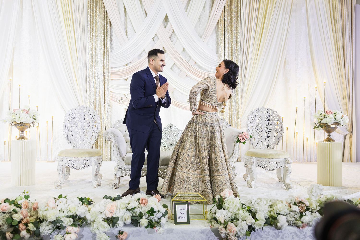Elegant white and gold wedding stage setup with floral arrangements and draped fabric.