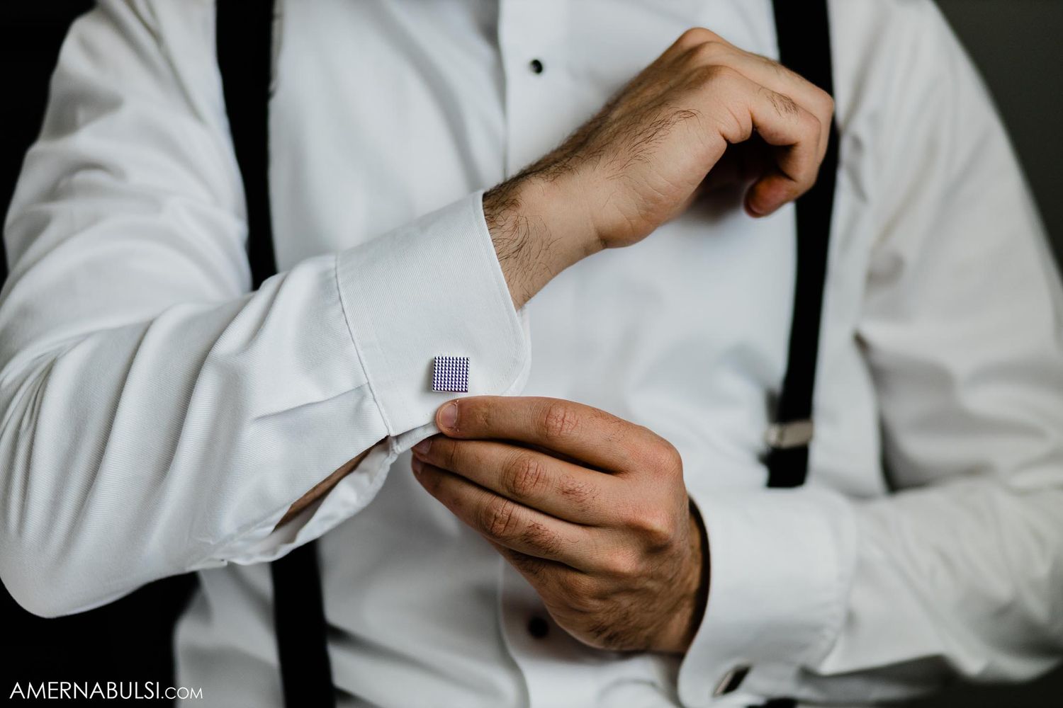 Close-up of formal attire showing hands adjusting white dress shirt cuffs with suspenders.