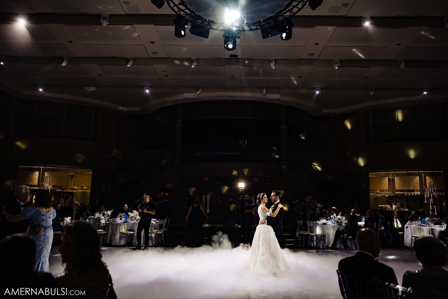 Wedding couple dancing on a fog-filled dance floor in a dimly lit reception venue.