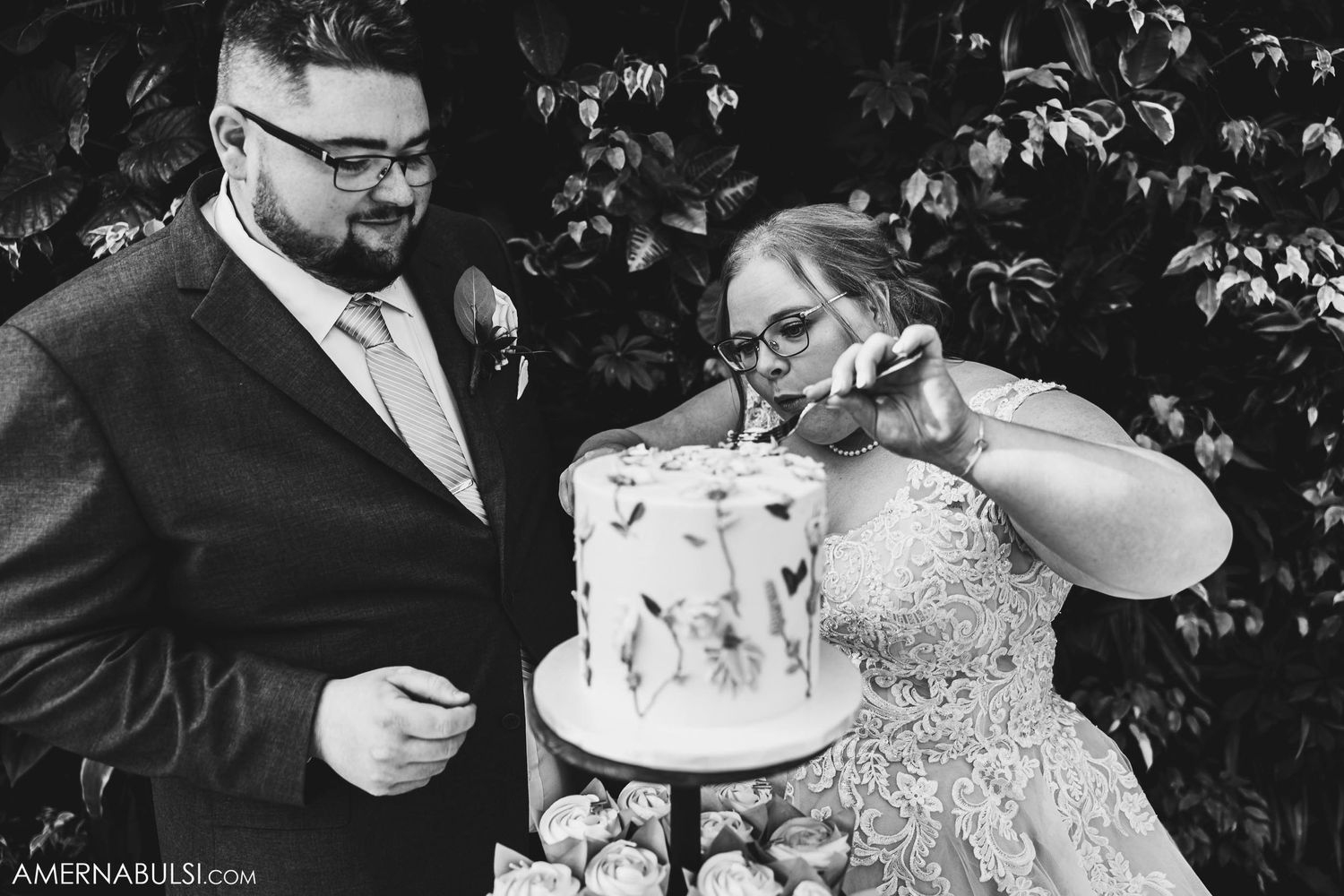 A couple share a sweet moment cutting their wedding cake with floral decorations at their reception.