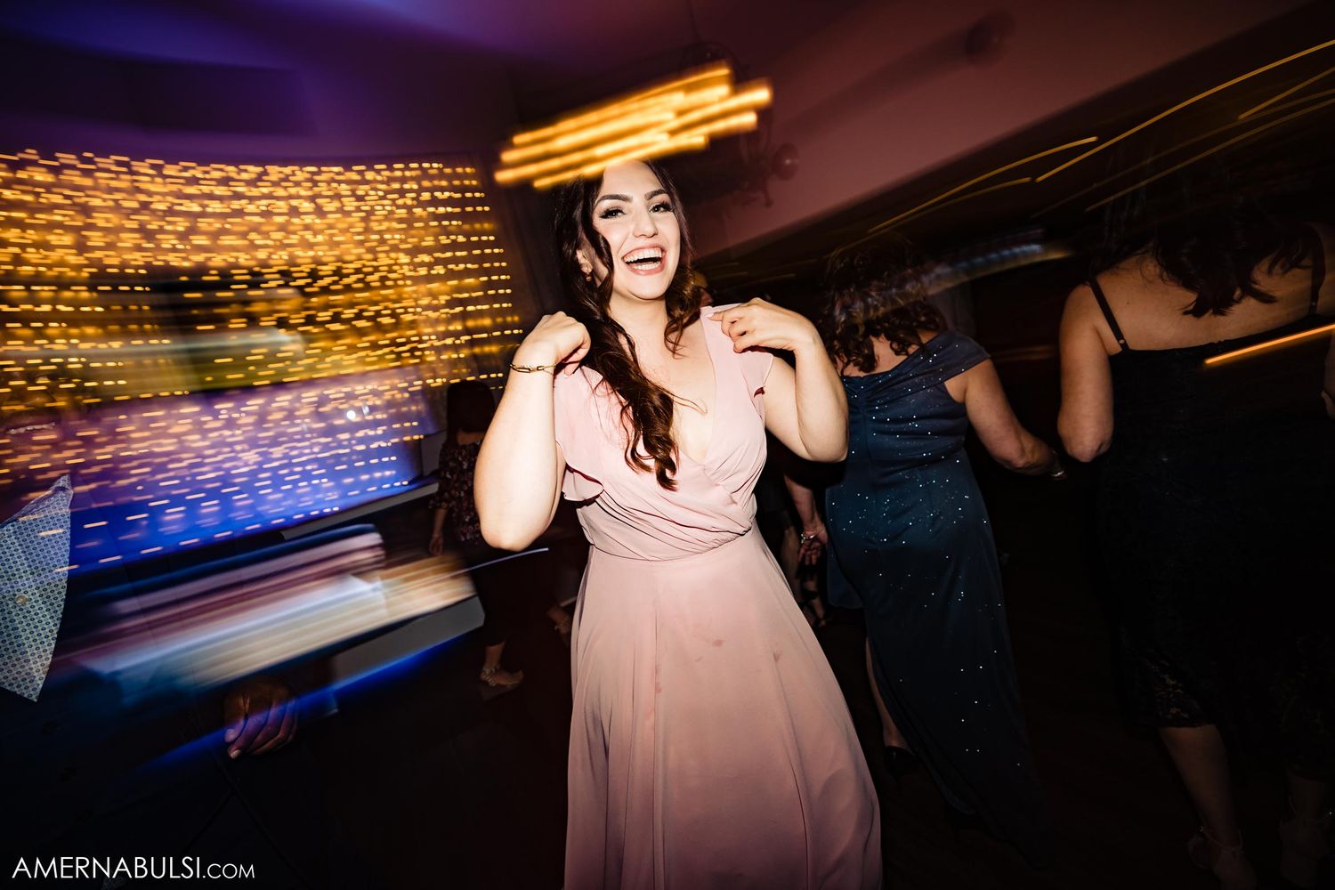 A guest in a pink dress dances joyfully at a wedding reception.