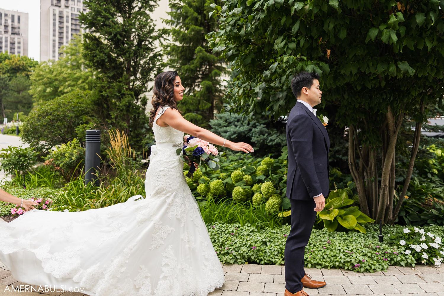 First look moment with bride tapping groom's shoulder in garden setting.