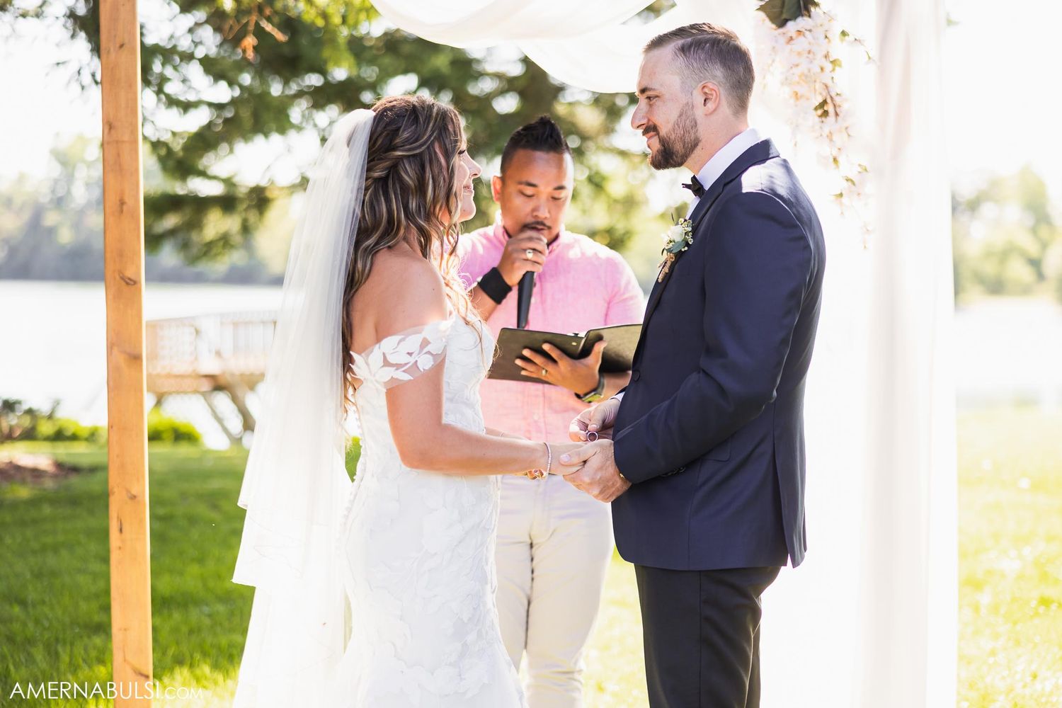 A couple exchanges wedding vows during their outdoor ceremony under a decorated wooden arch.