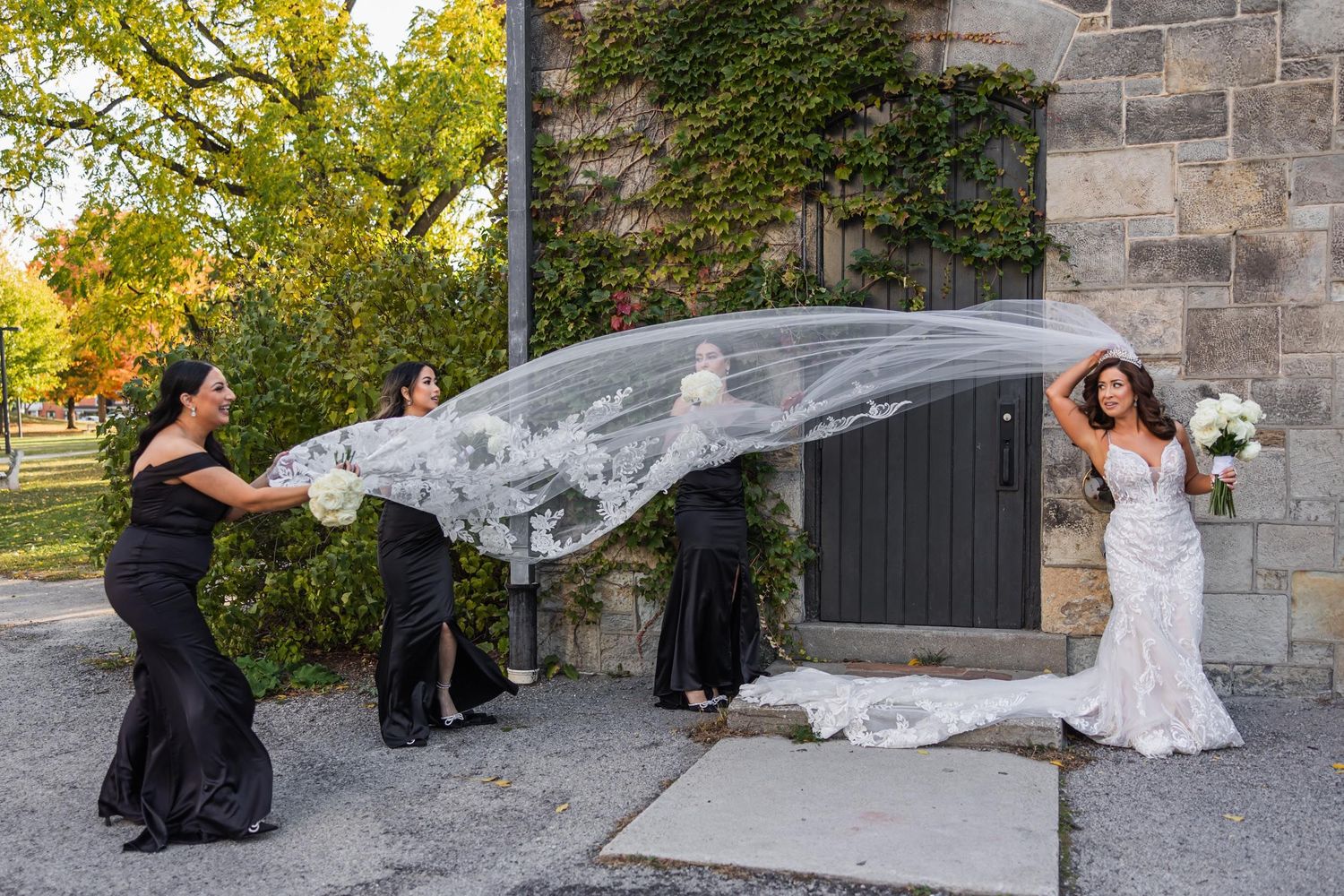 Wedding party members playfully toss a veil in an outdoor setting.