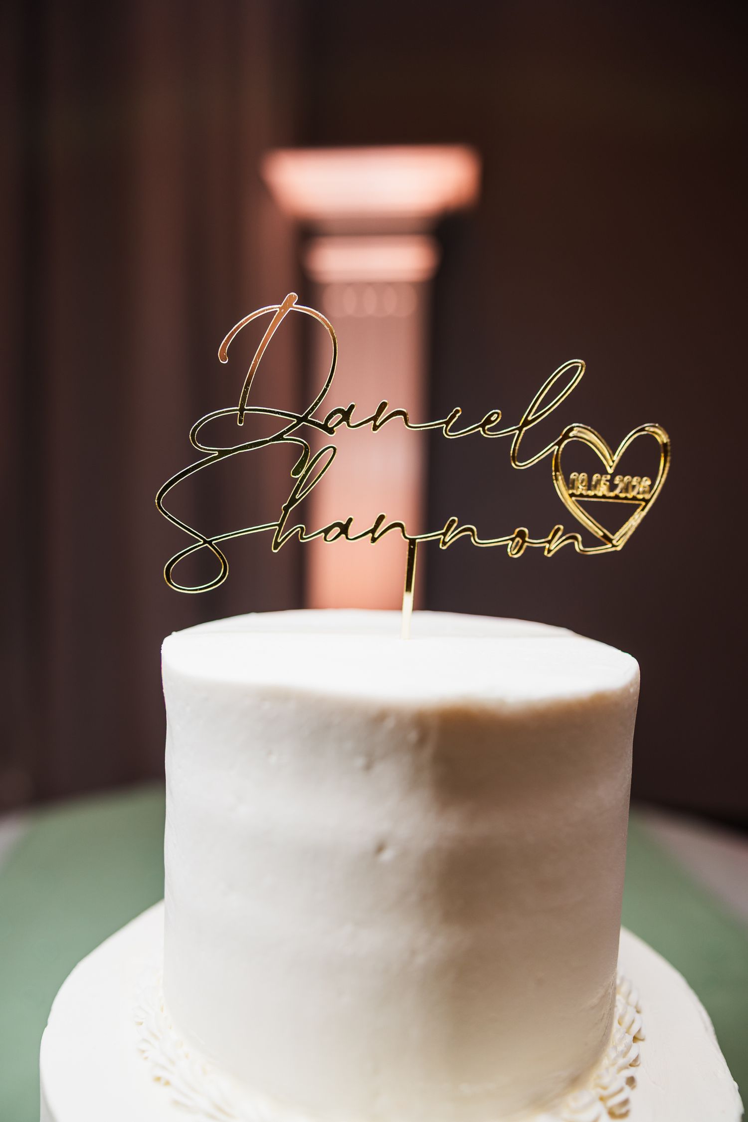 White wedding cake topped with gold mirror acrylic topper reading Daniel and Shannon with wedding date.