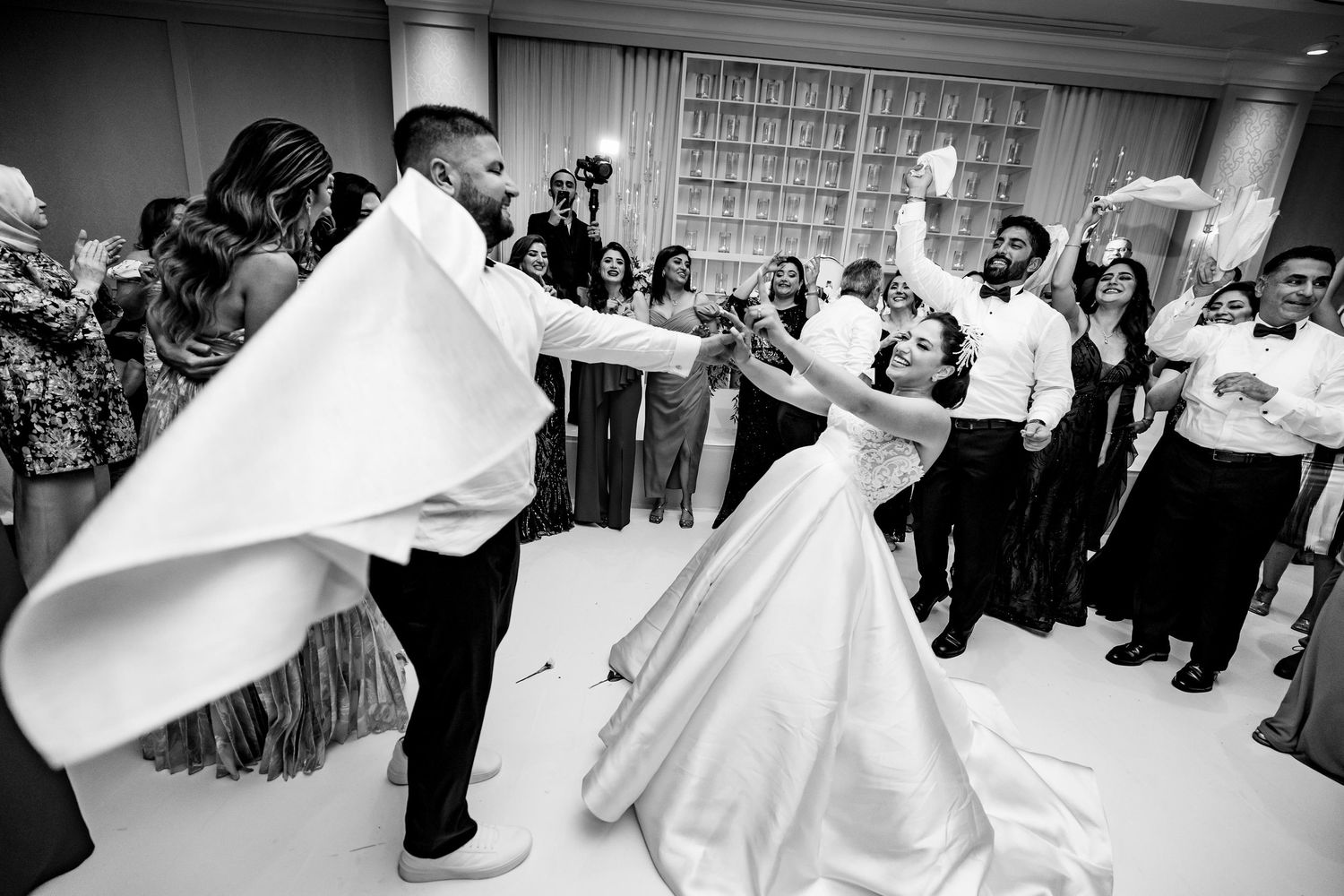 Wedding party dancing and celebrating on dance floor at indoor reception venue.