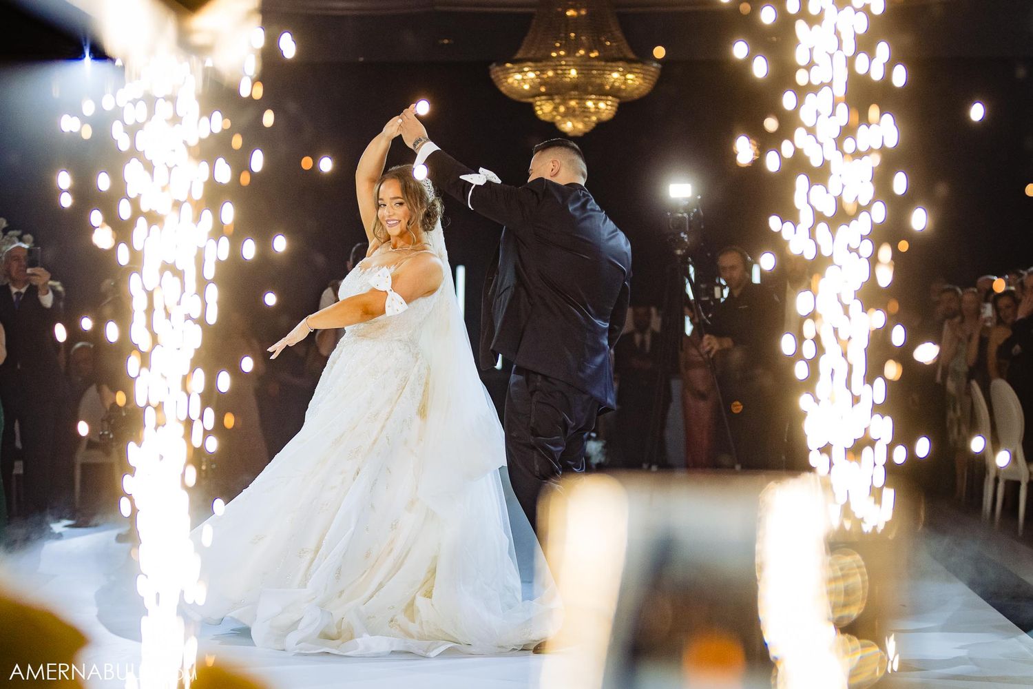 Couple dancing on white floor with dramatic sparkler fountains in background.