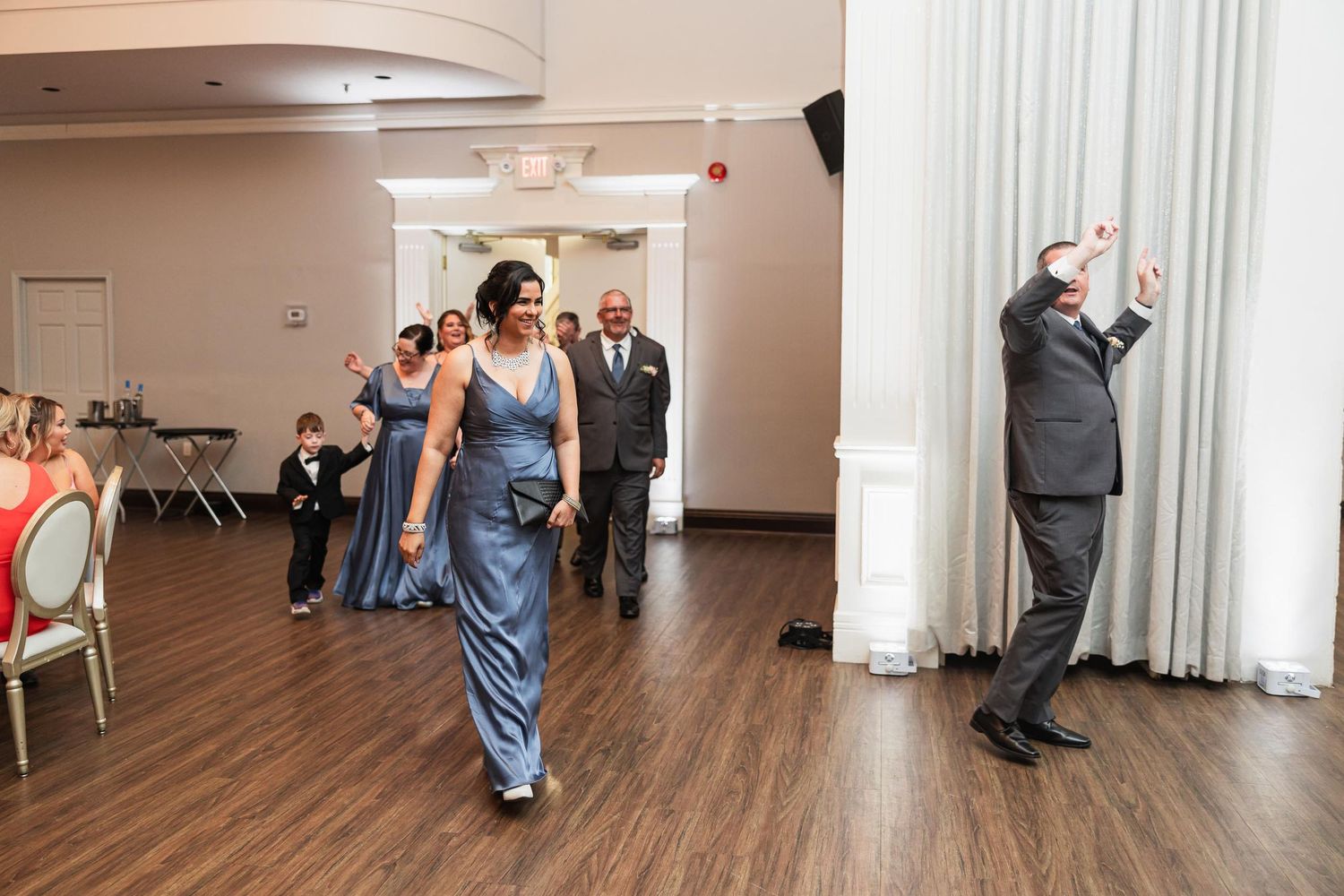 Wedding party members walking into reception hall with guests celebrating.