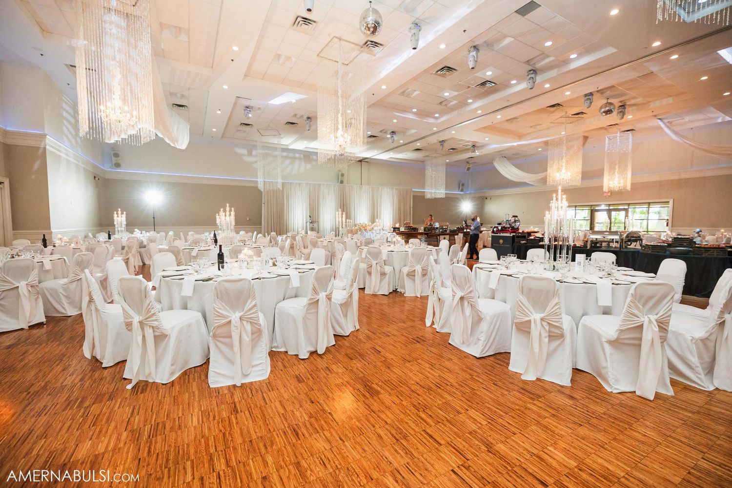 Spacious wedding reception venue with white-covered chairs and crystal chandeliers.
