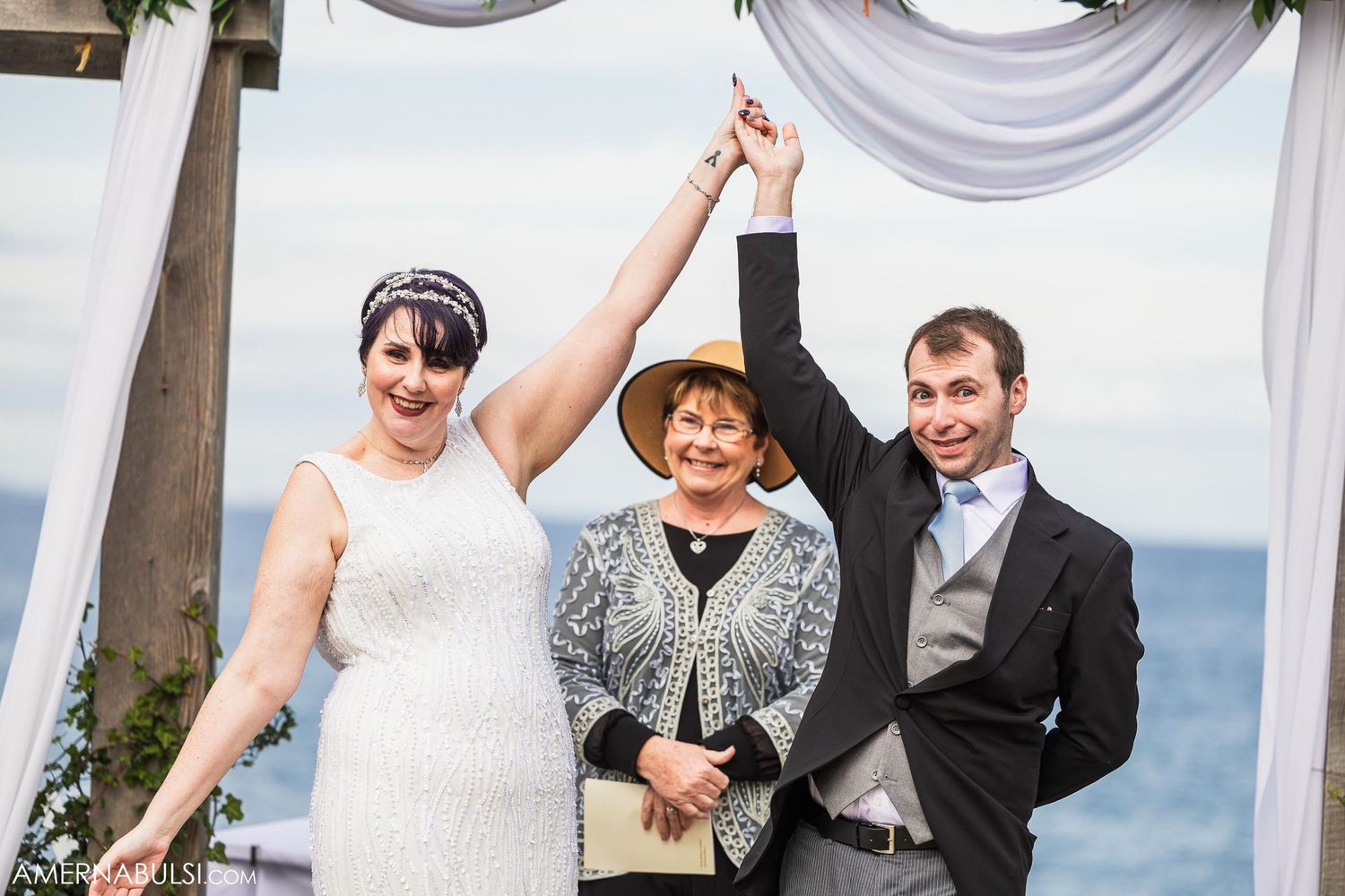 A celebratory outdoor wedding ceremony moment under a decorated pergola by the ocean.