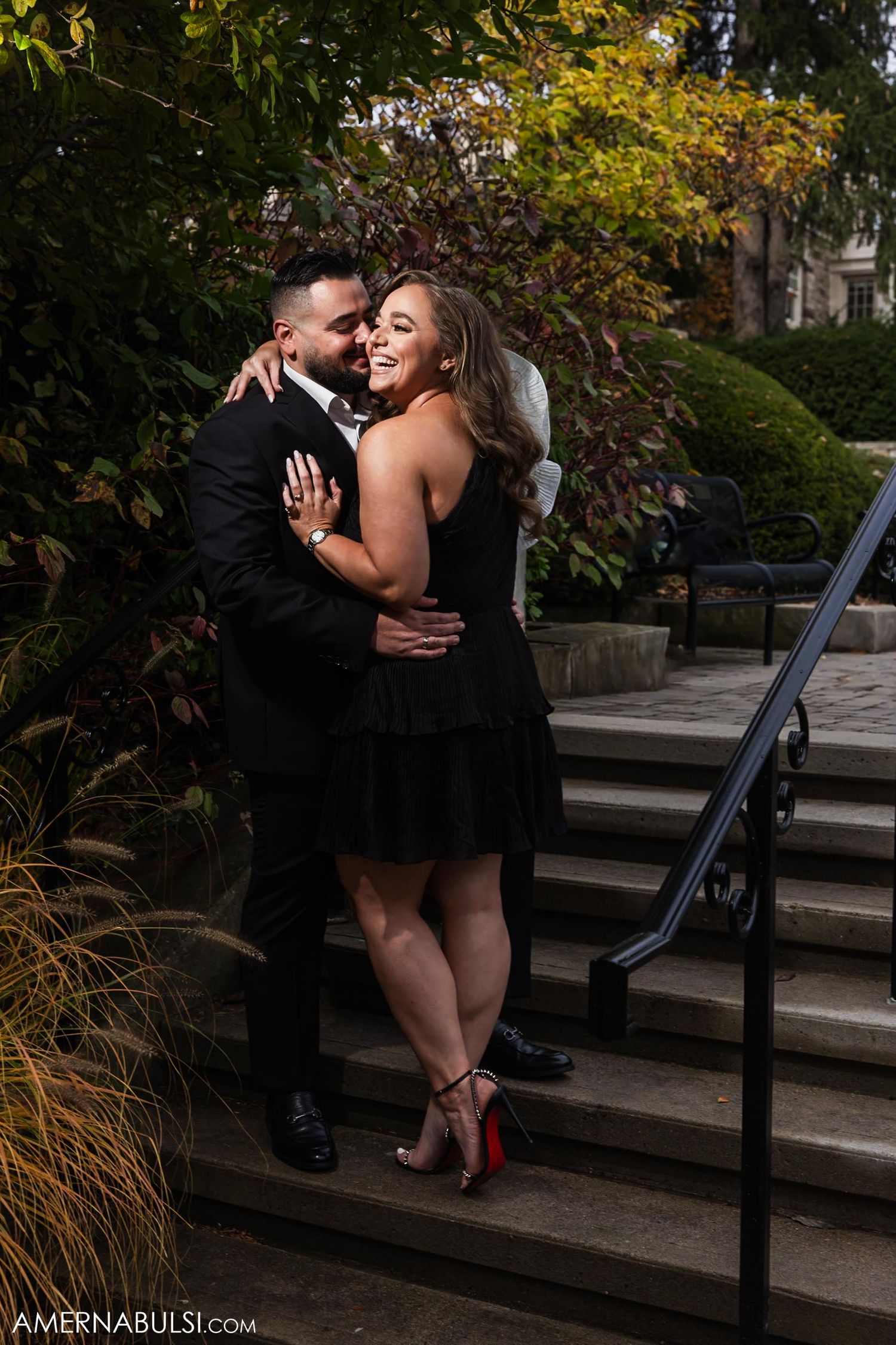 Joyful couple in black formal wear sharing intimate moment on outdoor steps.
