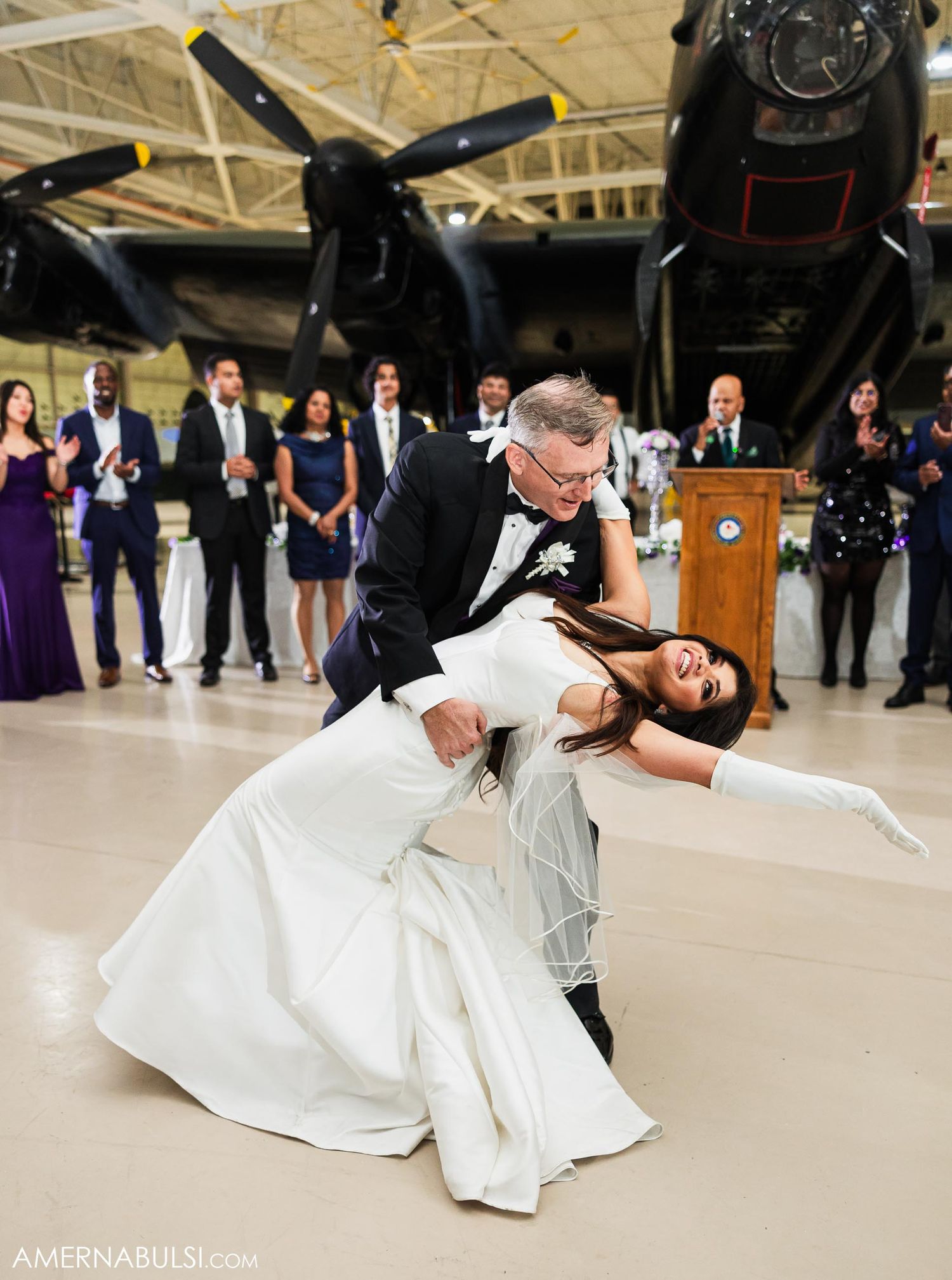 Dramatic dip during wedding dance performance in an aircraft hangar with guests watching.