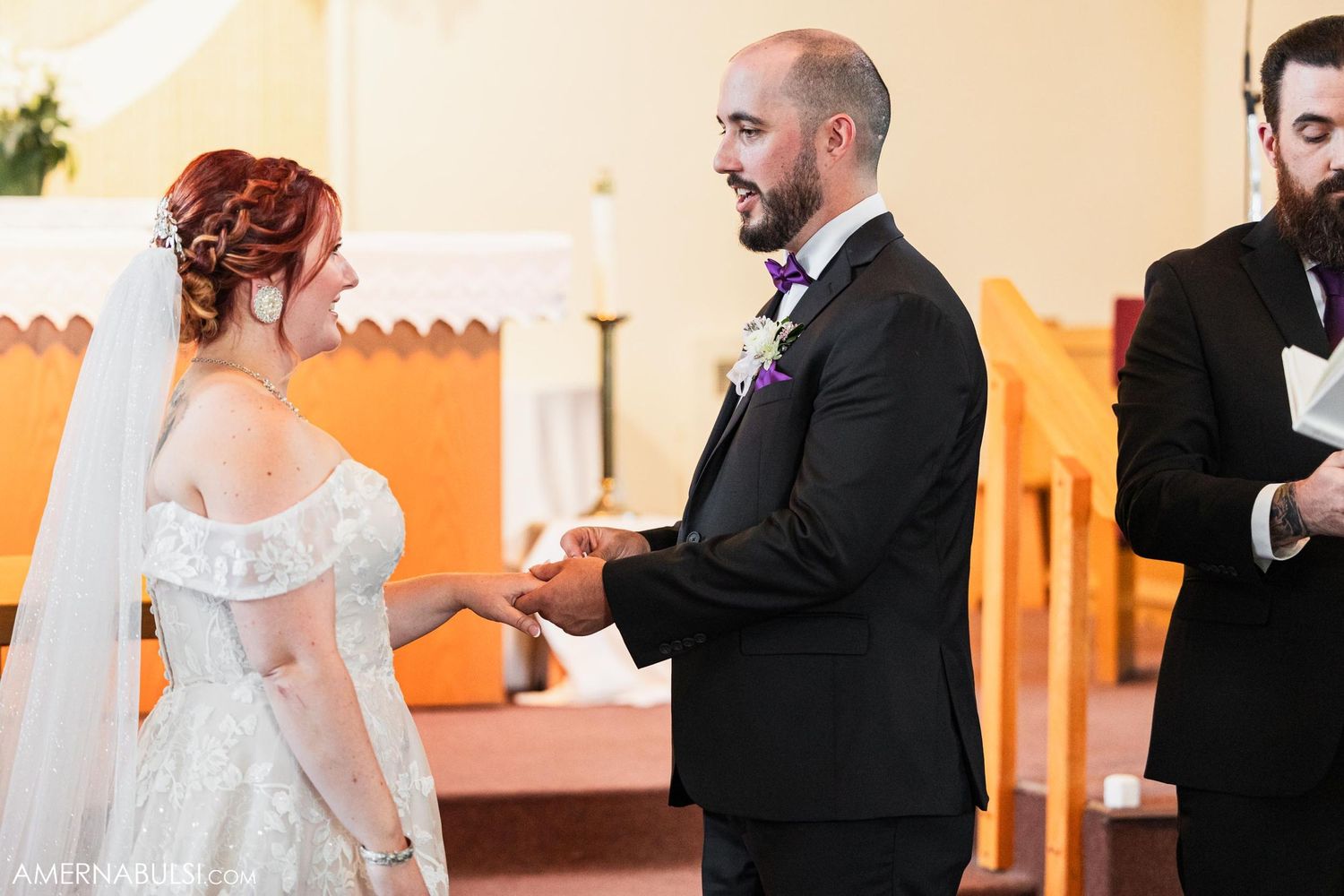 Couple exchanging rings during wedding ceremony with orange walls and white decor in background.