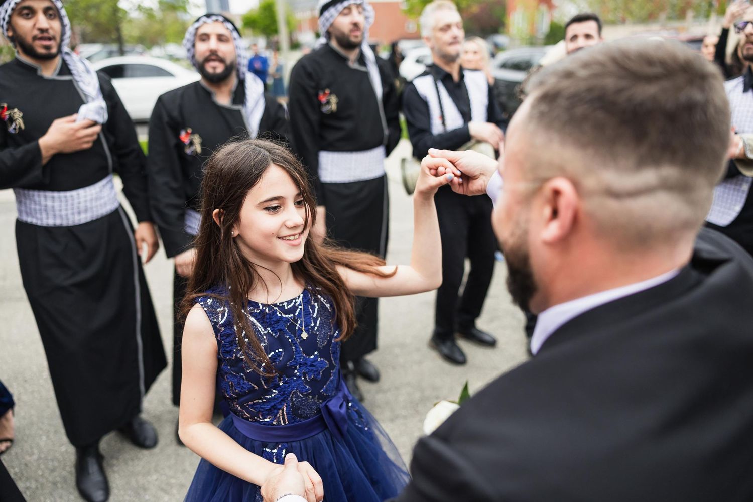 A young girl in a blue dress dances during an outdoor celebration.