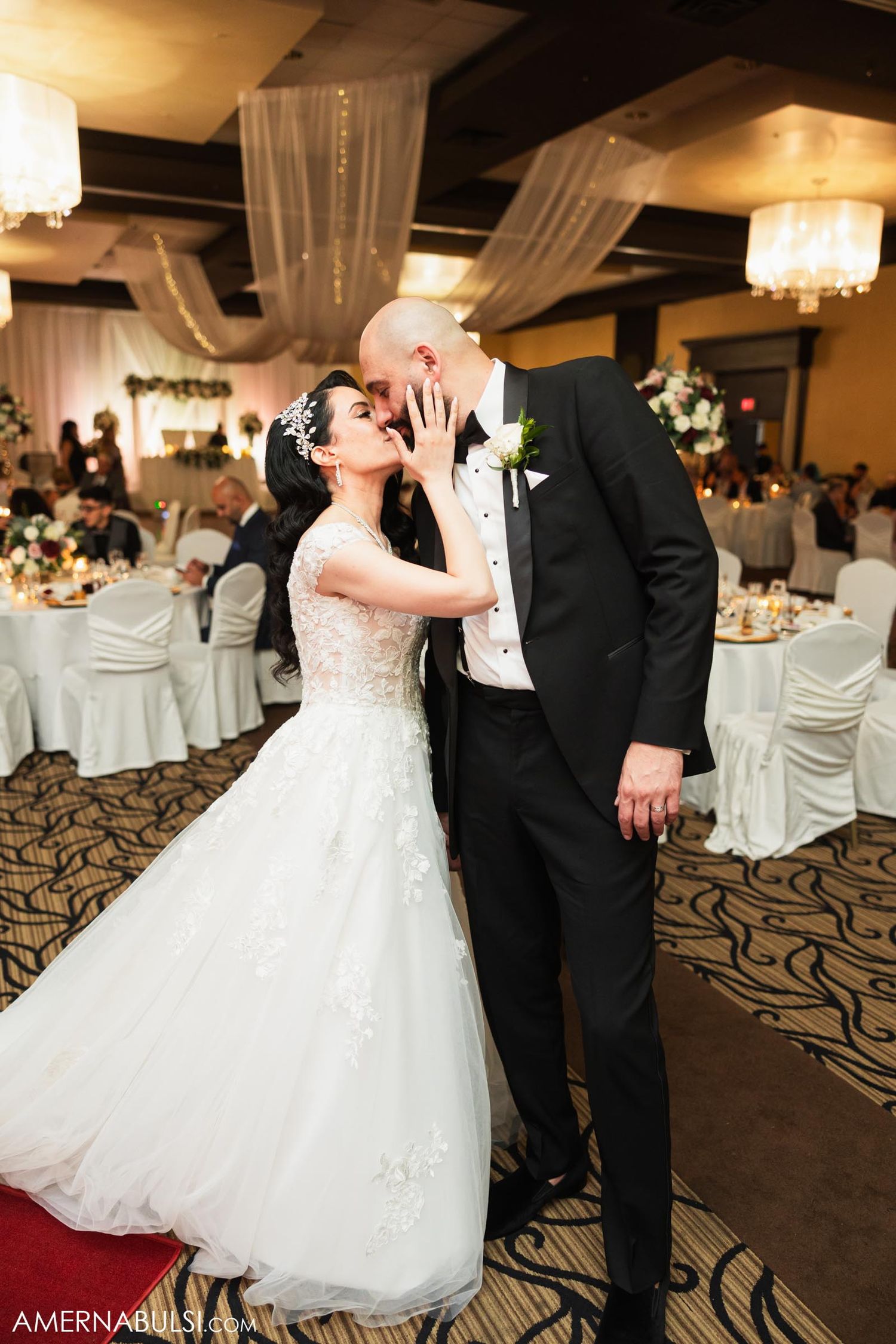 Reception moment in an elegant ballroom with decorative ceiling drapes and chandeliers.