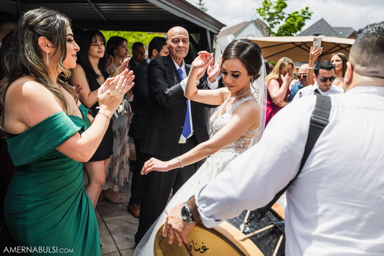 Wedding guests clapping and celebrating while musicians perform at an outdoor reception.