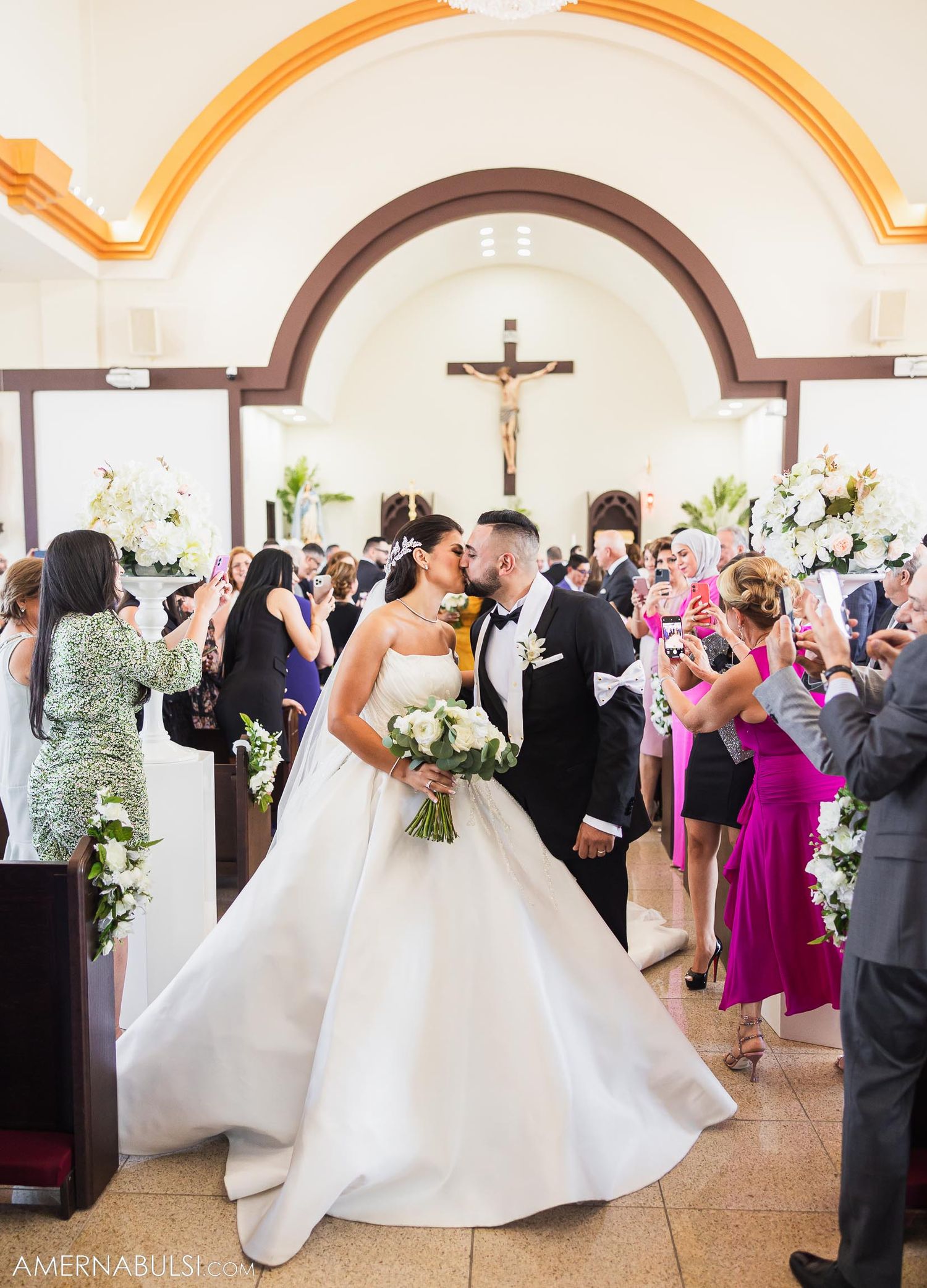 Wedding celebration in church with guests capturing moment on phones as couple shares romantic moment.
