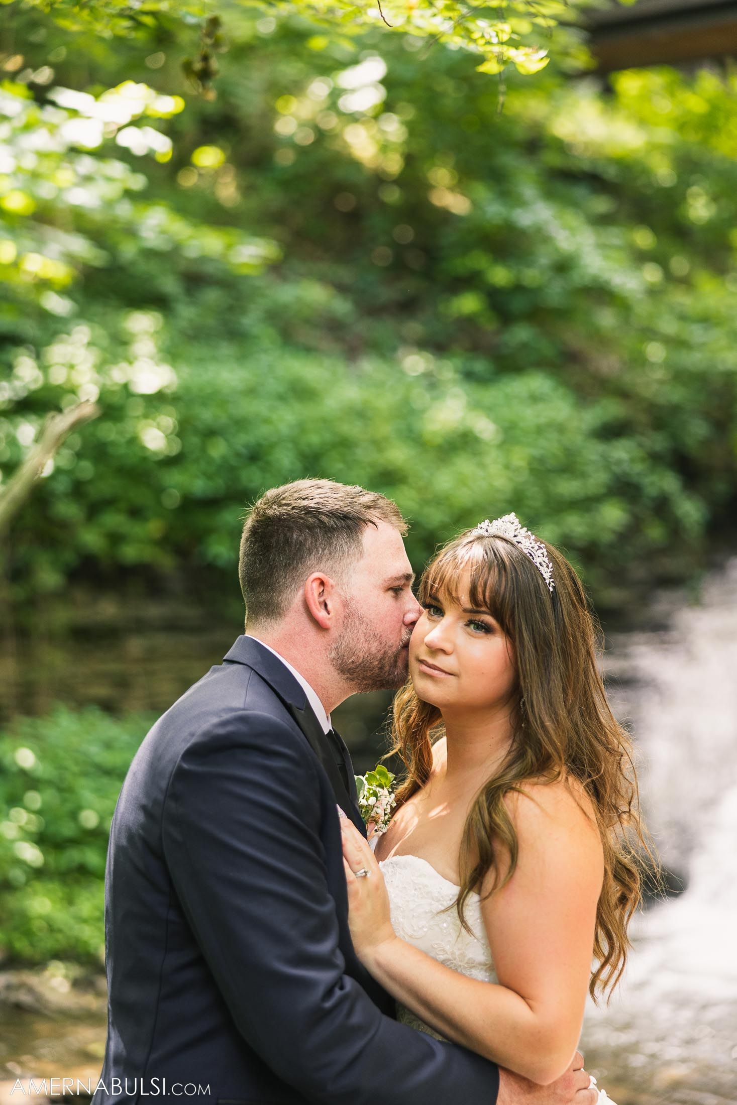 Intimate wedding portrait of couple in formal attire against green natural background.