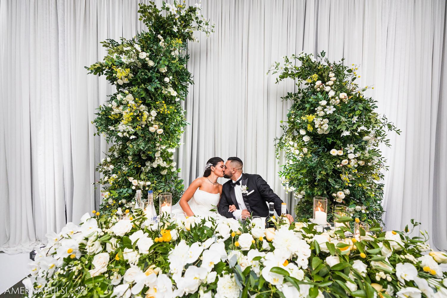 Elegant wedding altar arch decorated with lush white flowers and greenery against a white draped backdrop.