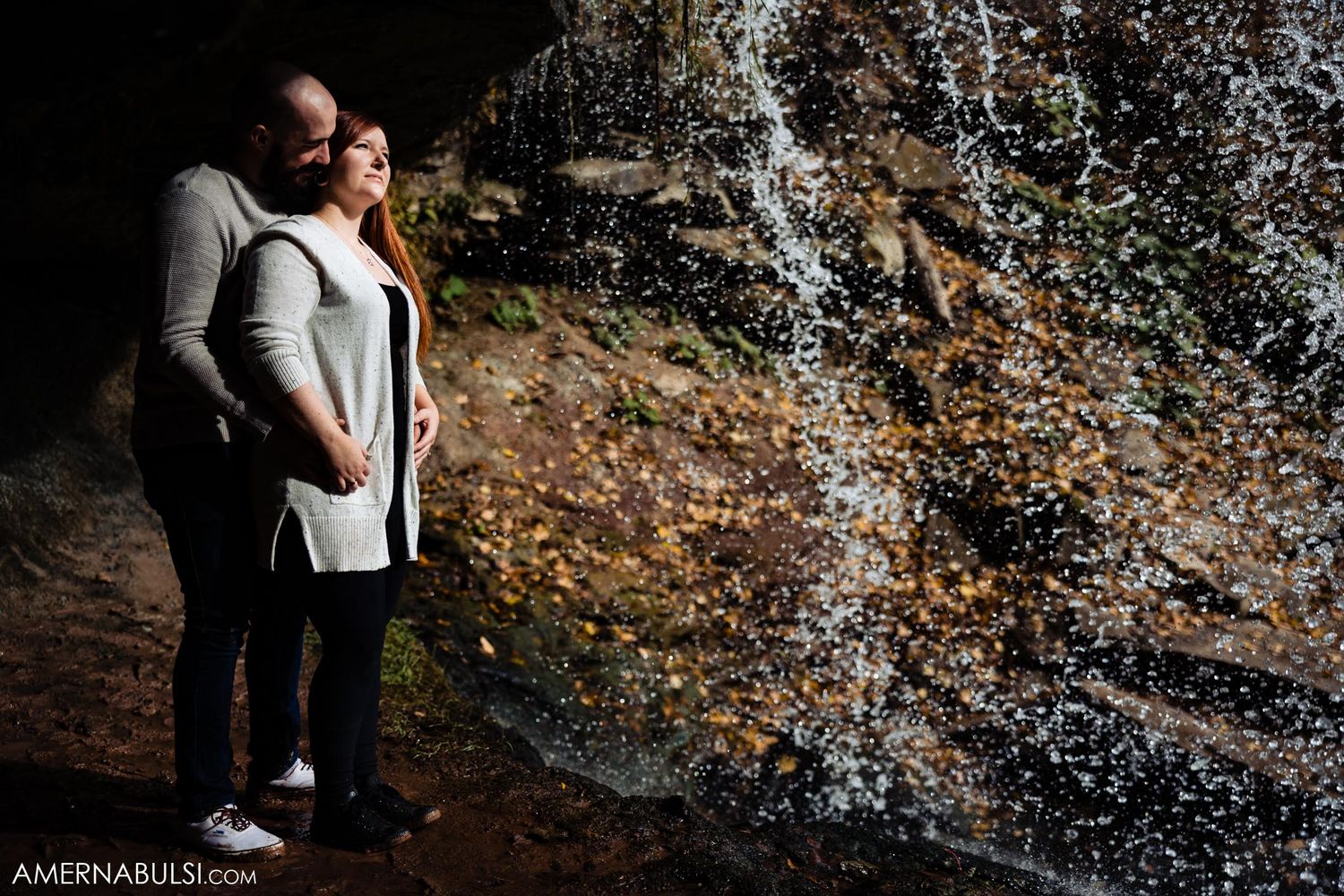 Couple standing by misty waterfall surrounded by autumn scenery.