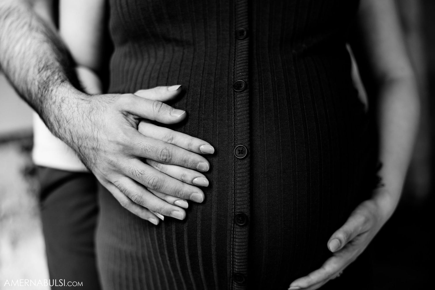 Black and white close-up of hands embracing pregnant belly.
