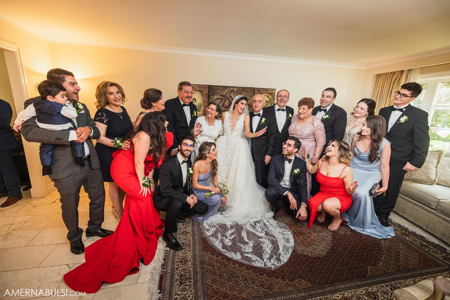 Large wedding party poses for formal group photo in elegant living room setting.