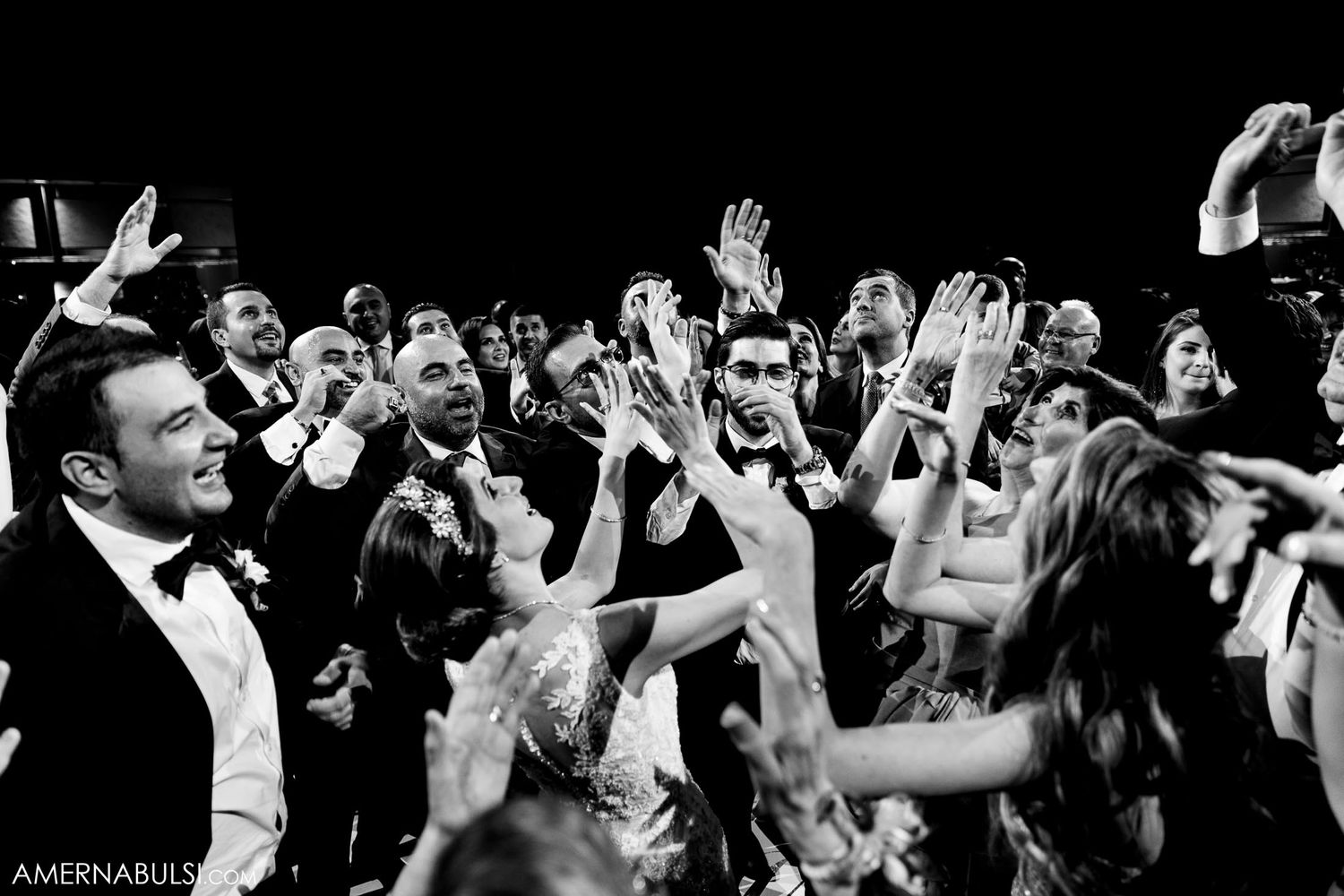 Black and white photo of wedding guests dancing with hands raised at reception party.