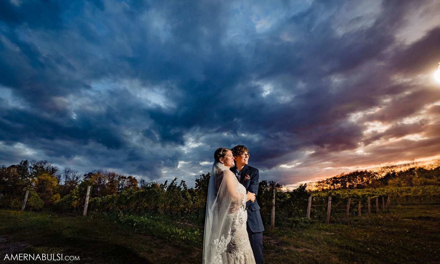 Dramatic sunset wedding photo in vineyard with stormy purple and orange sky.