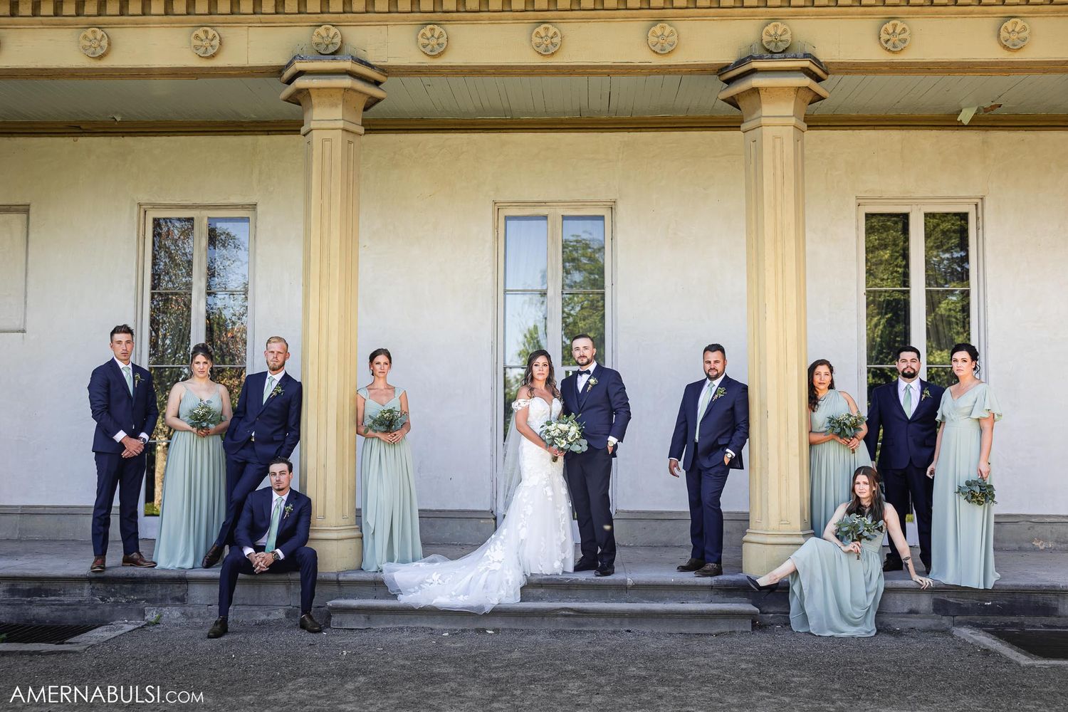 Wedding party poses on grand steps with bridesmaids in sage green dresses.
