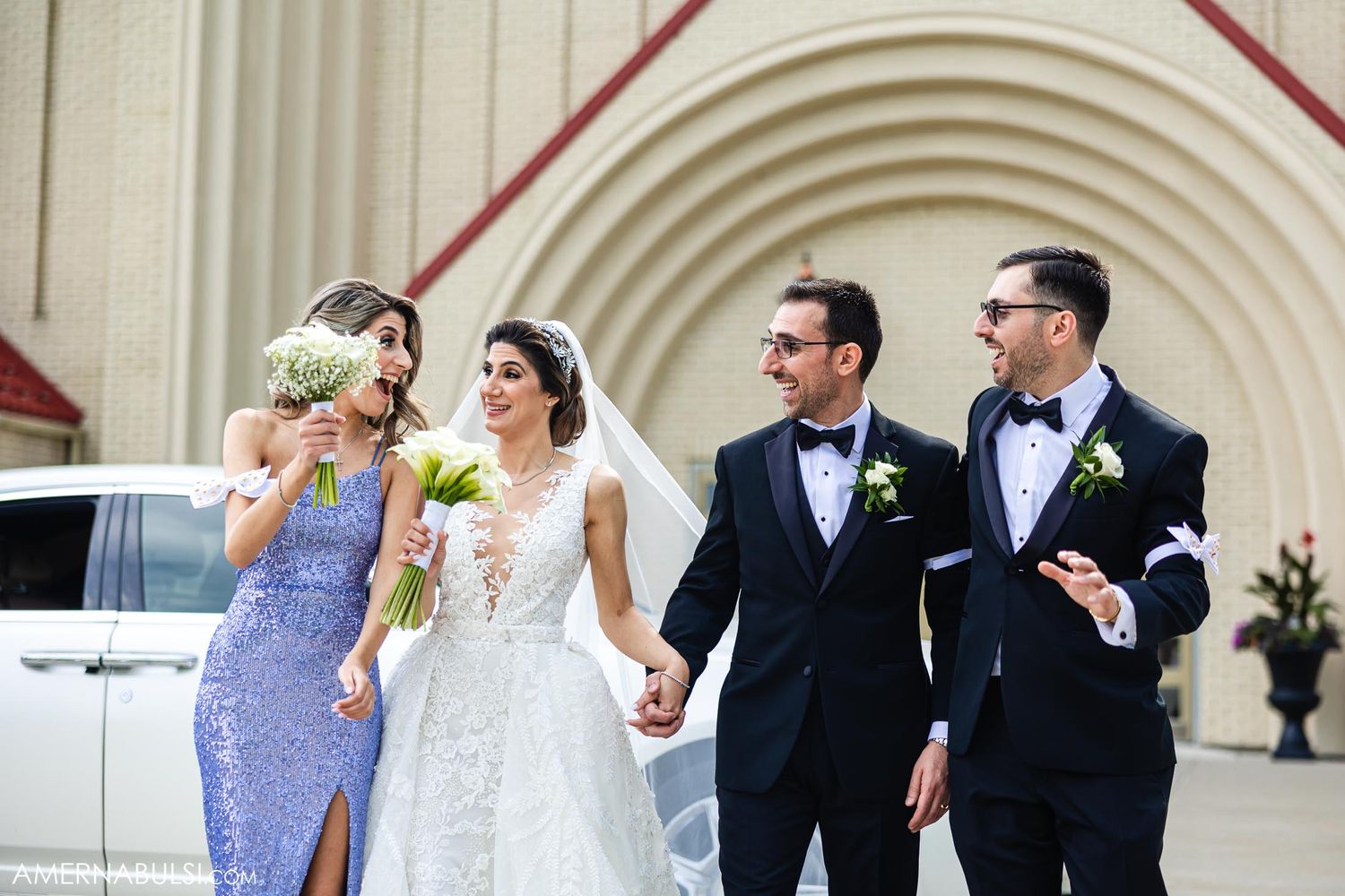 Wedding party celebrating together outside church with white limousine in background.