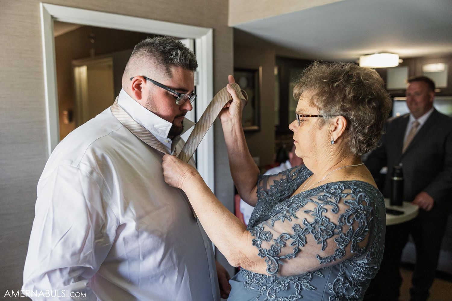 Woman in lace dress helping to adjust a man's formal attire before an event.