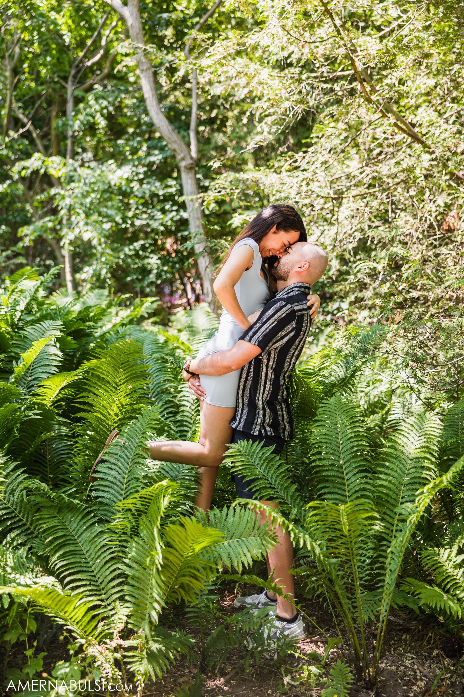 A tender embrace captured amidst towering ferns in a sunlit forest.